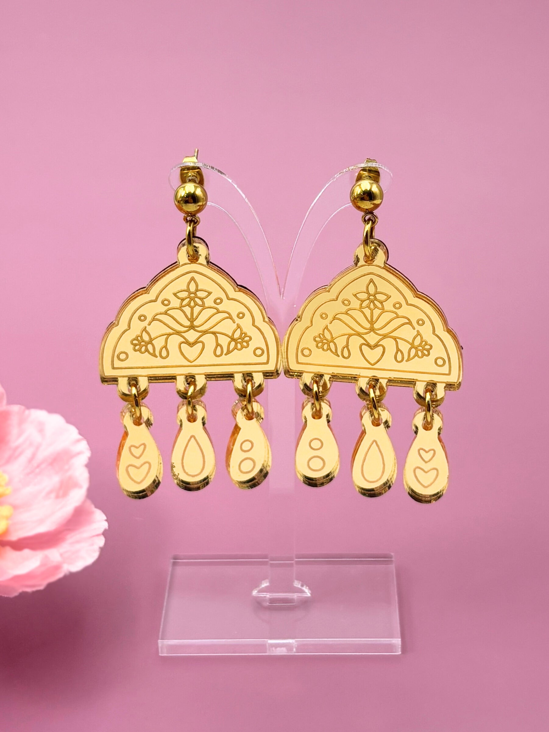 Gold earrings with intricate designs on a pink background