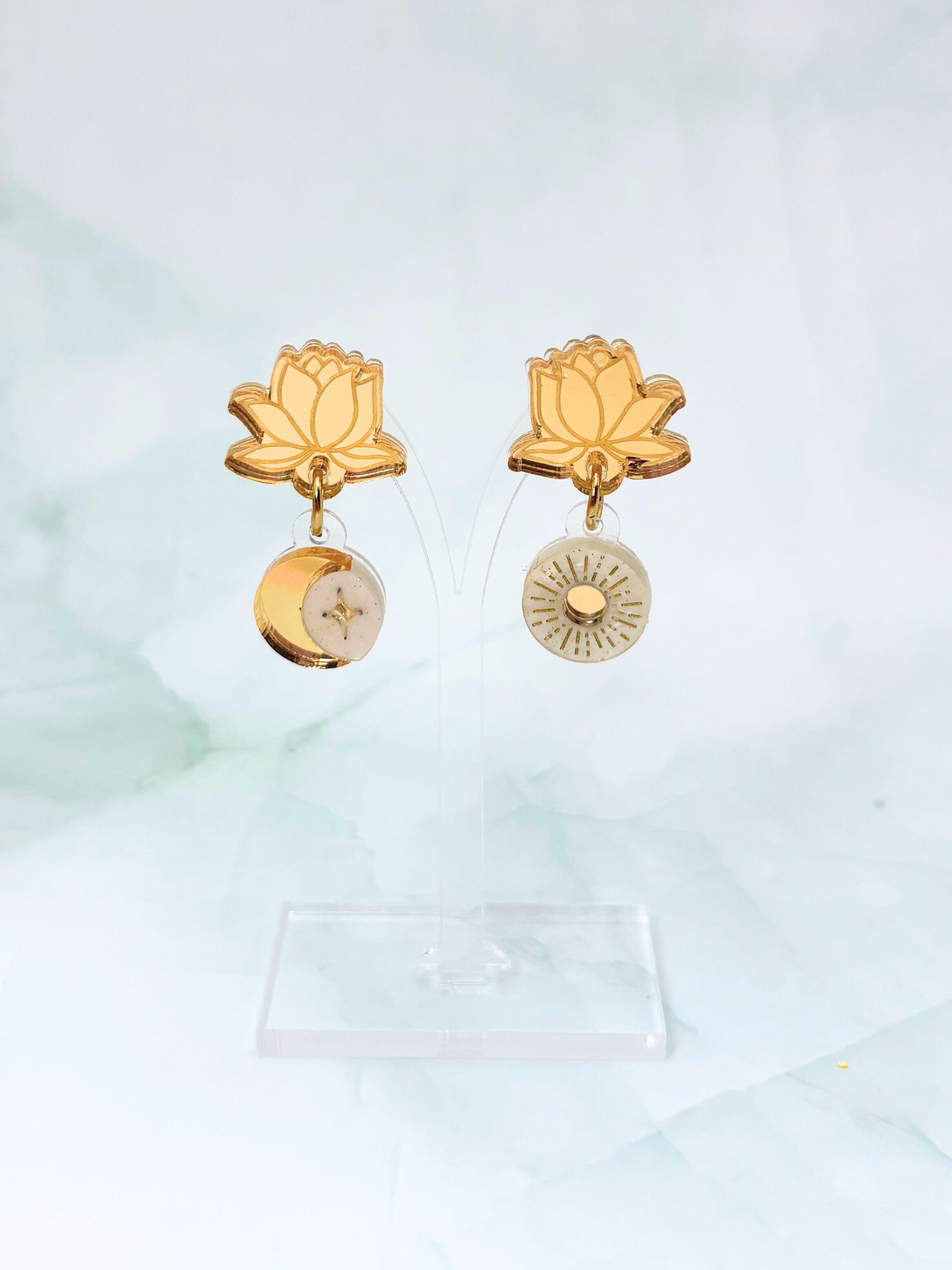 Gold lotus and moon earrings on a light green background