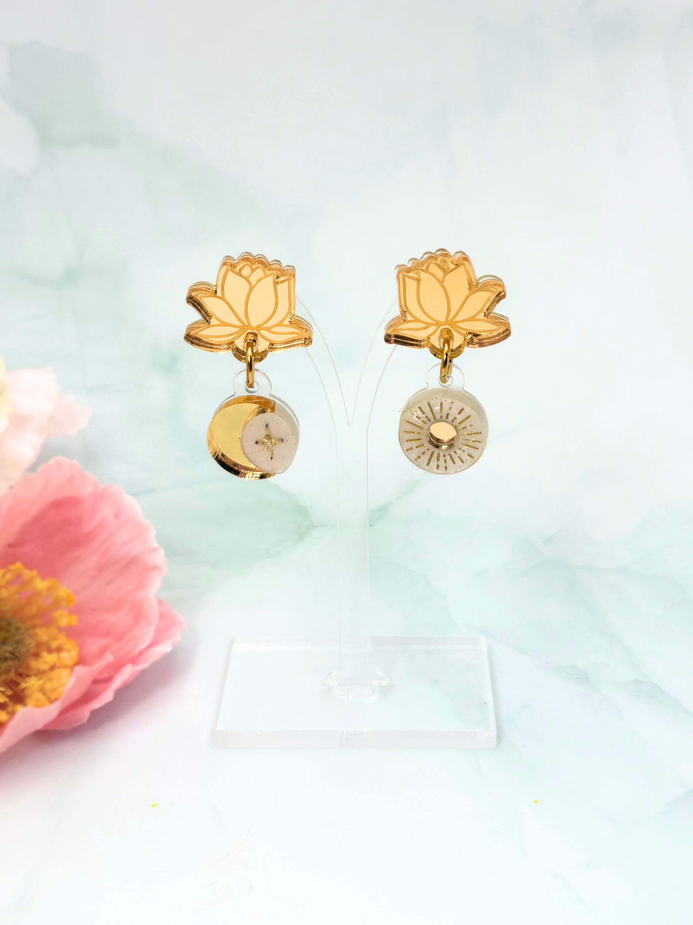 Gold lotus flower earrings on a light green background with pink flowers.