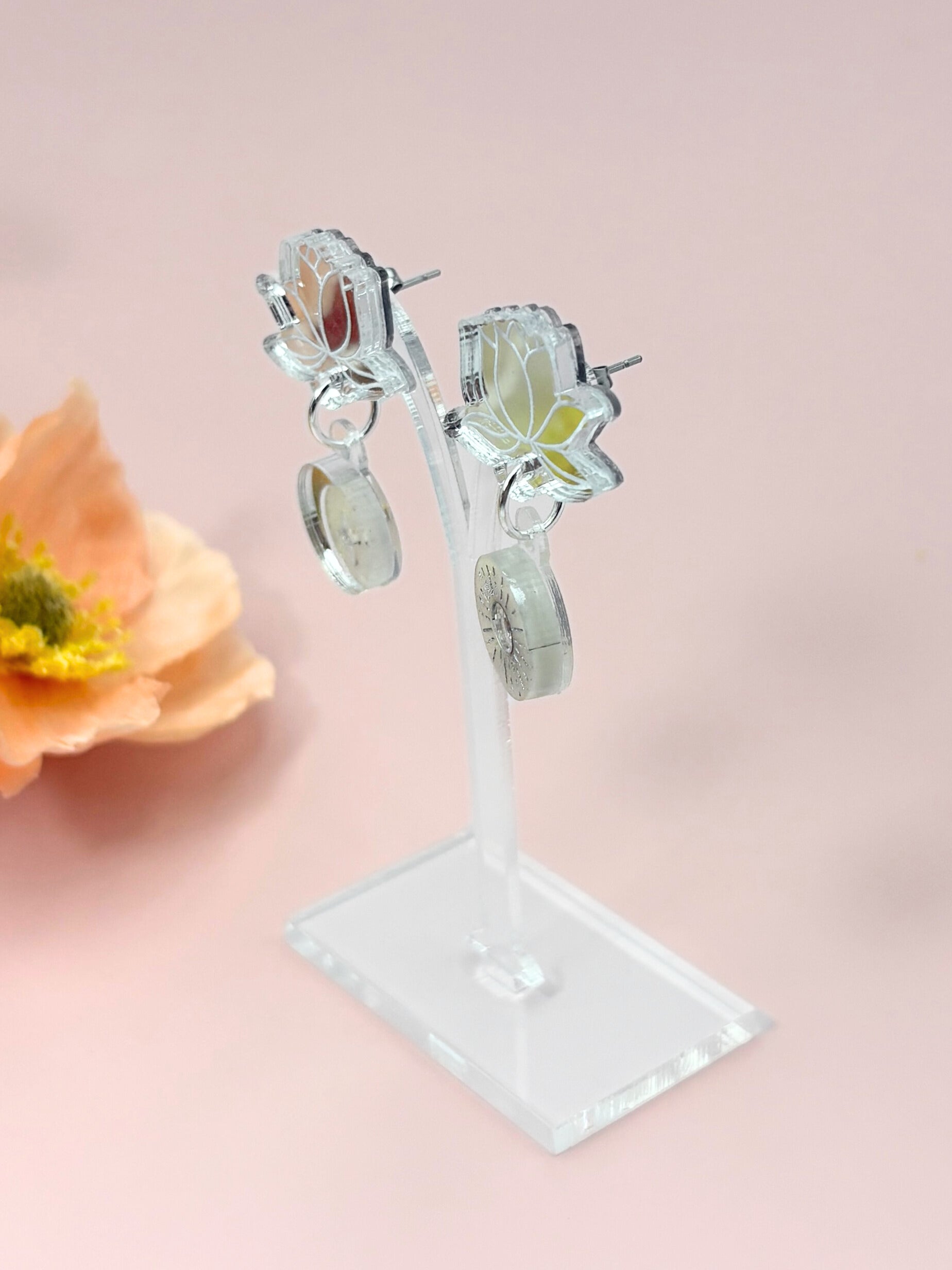 Pair of silver earrings on a stand with a pink background