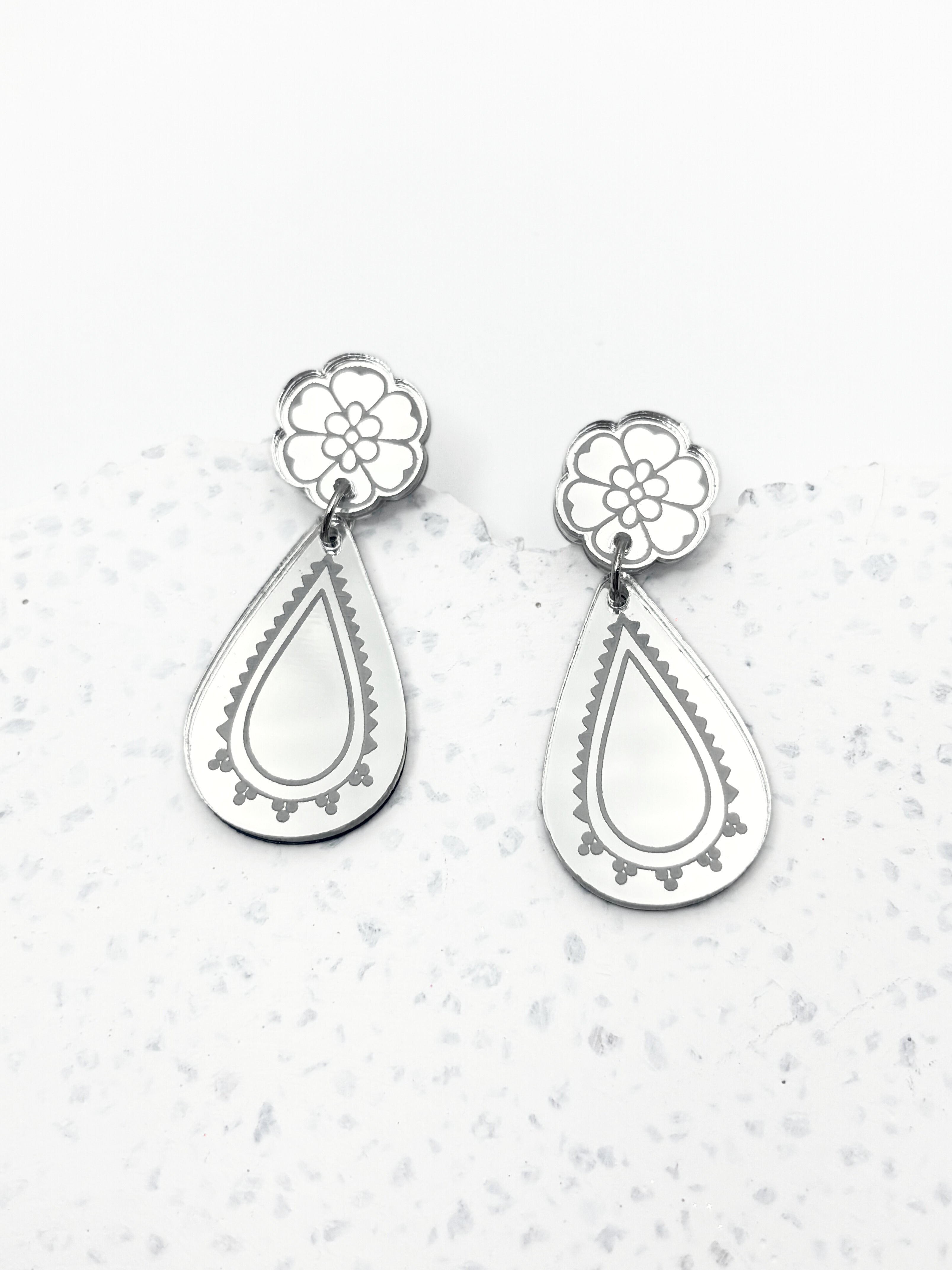 Silver teardrop earrings with floral tops on a light gray background