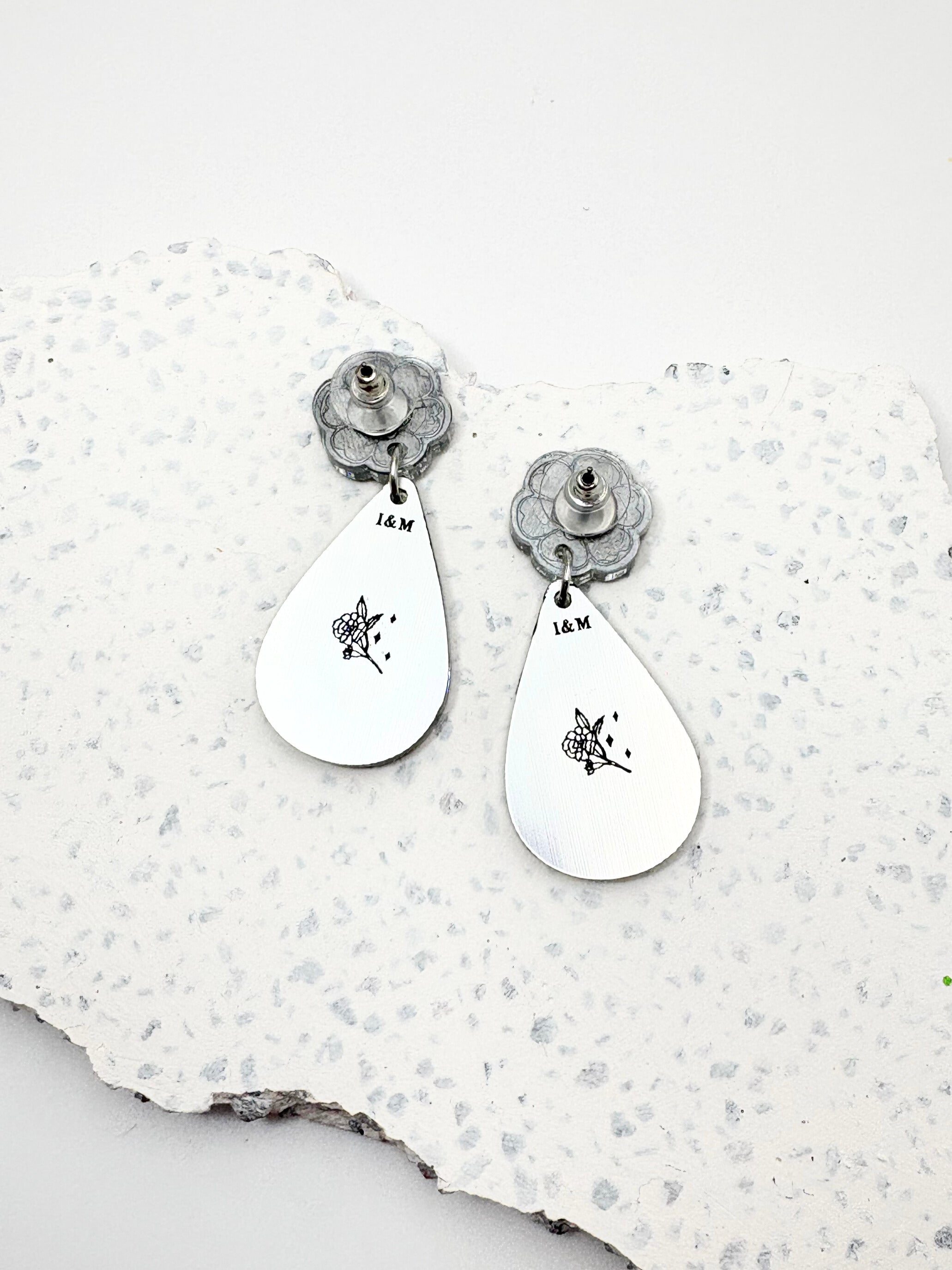 Pair of silver teardrop earrings with floral designs on a textured white surface