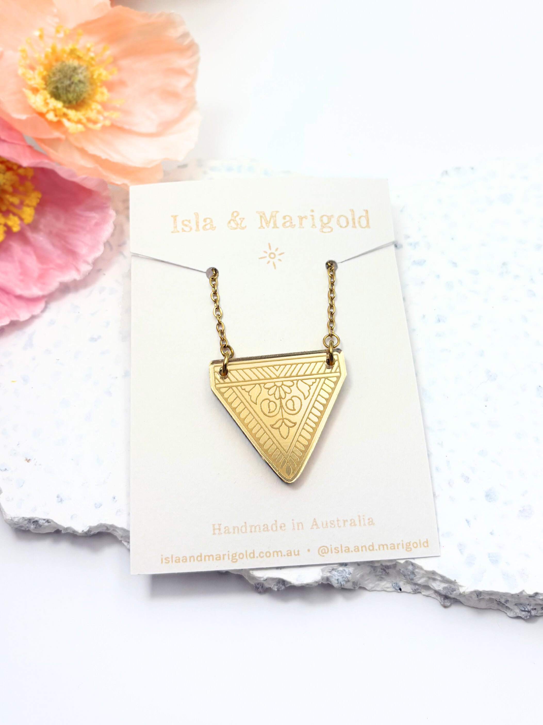 Gold triangle necklace on a Isla & Marigold card with flowers in the background