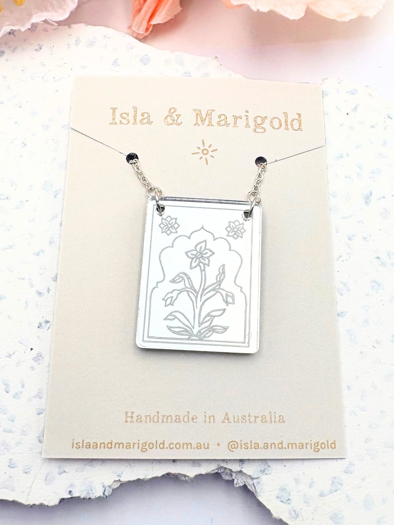 Silver necklace with floral design on a 'Isla & Marigold' card with flowers in the background