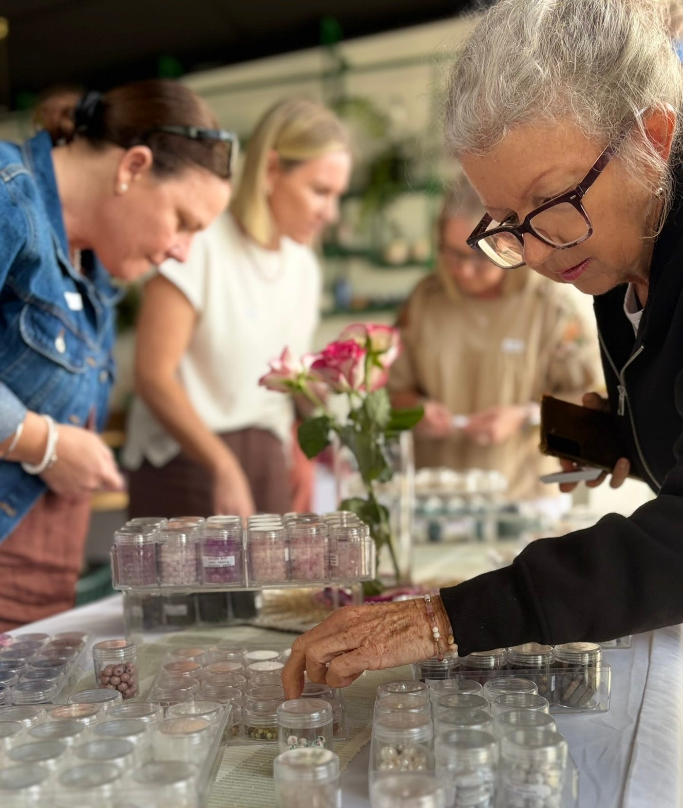 Several people gathered around a white table filled with small clear jars and trays containing pink and beige capsules or pills, with one woman in the foreground looking down at the items.