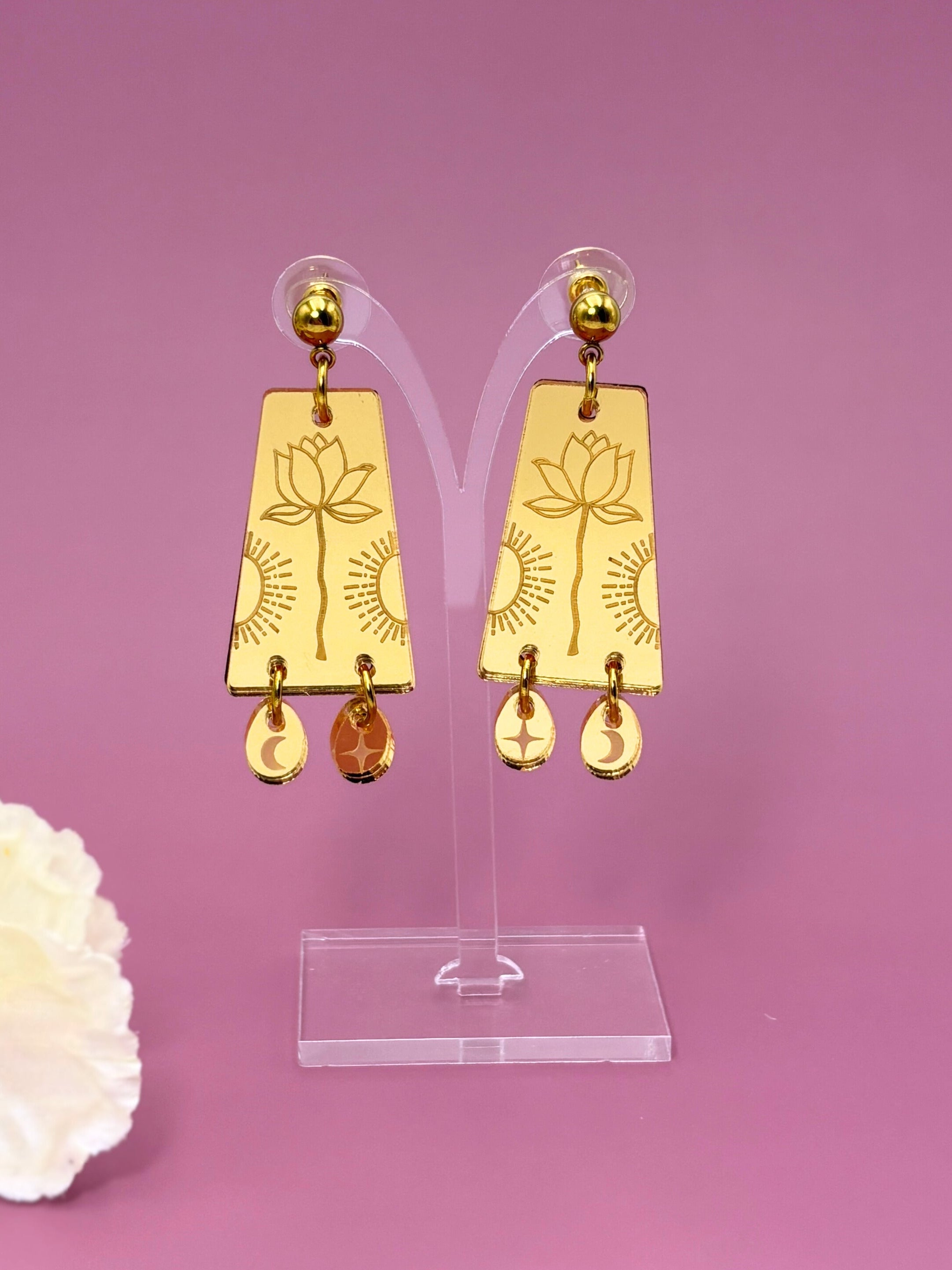Gold earrings on a clear stand with a pink background