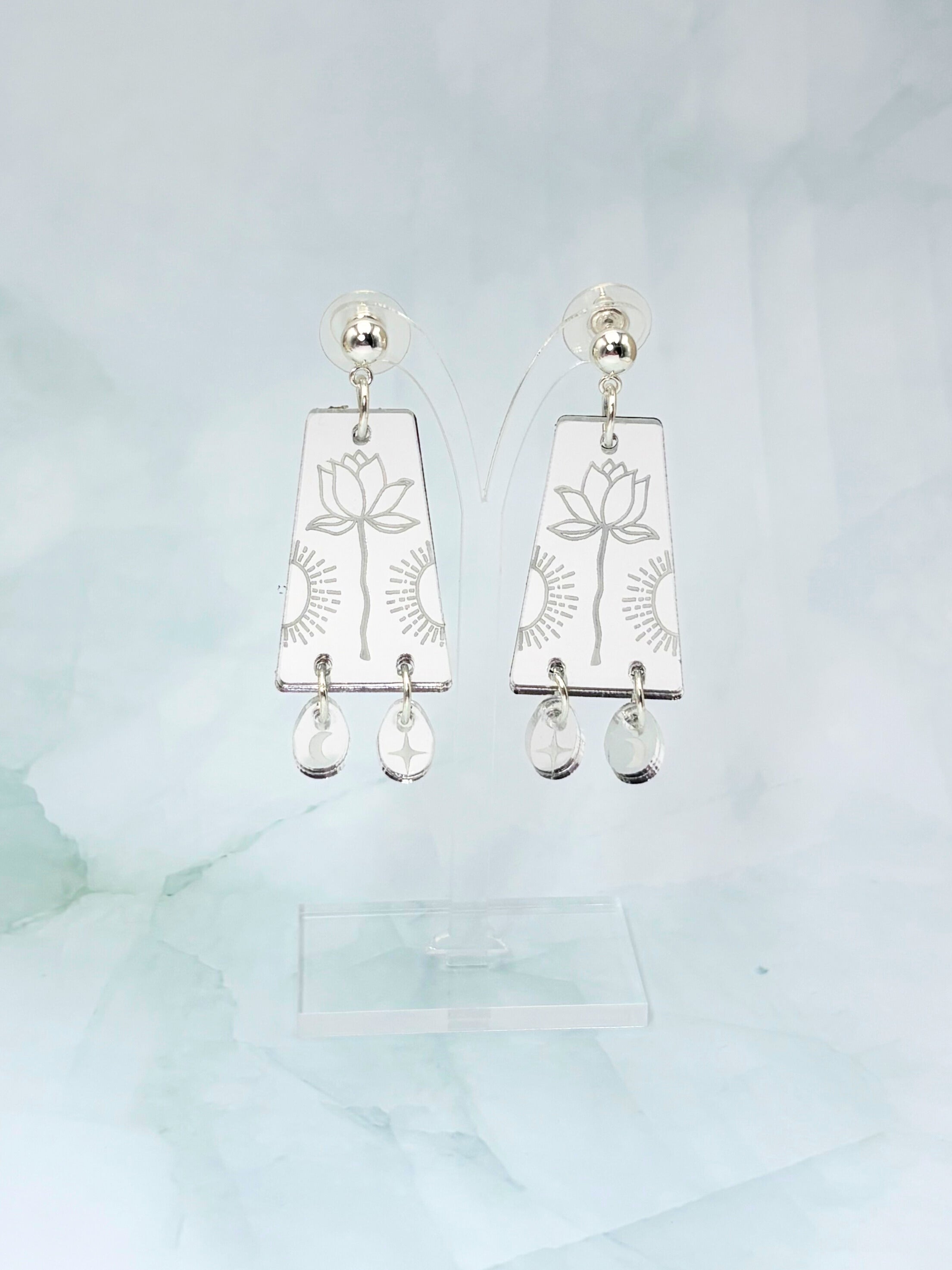 Silver earrings with floral designs and clear stones on a light blue background