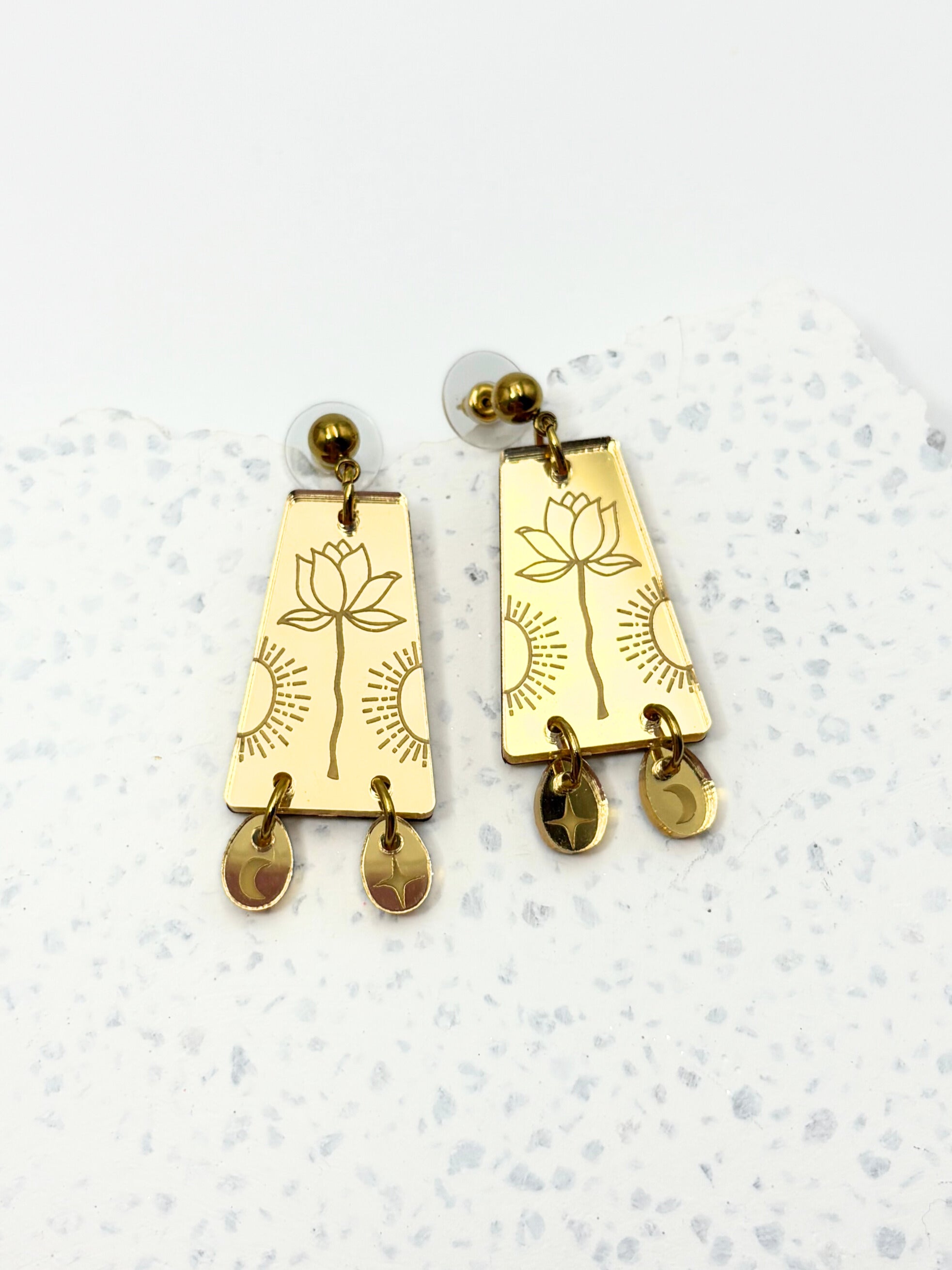 Gold earrings with lotus designs on a light gray background
