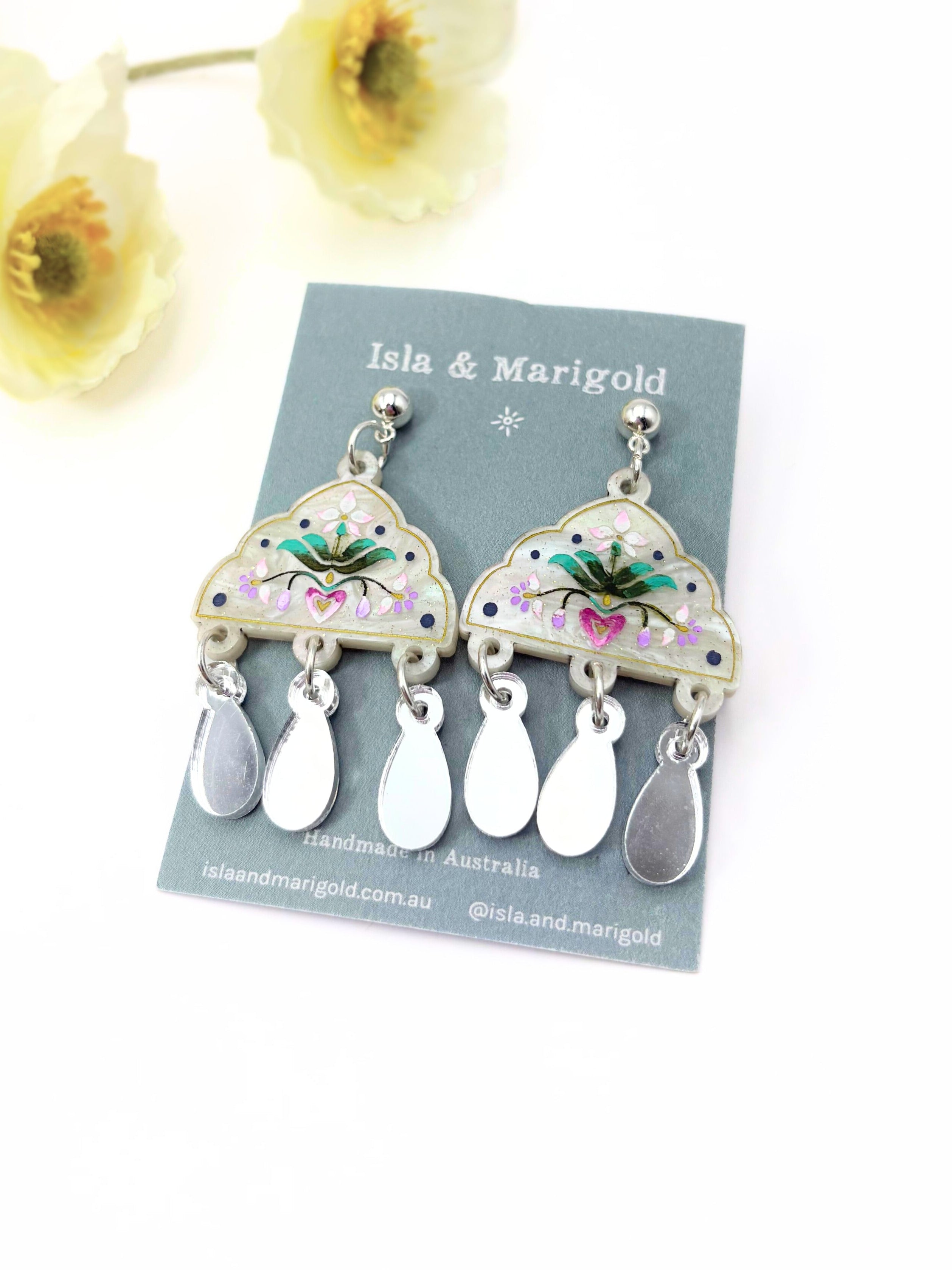 Pair of earrings on a 'Isla & Marigold' branded card with flowers in the background.