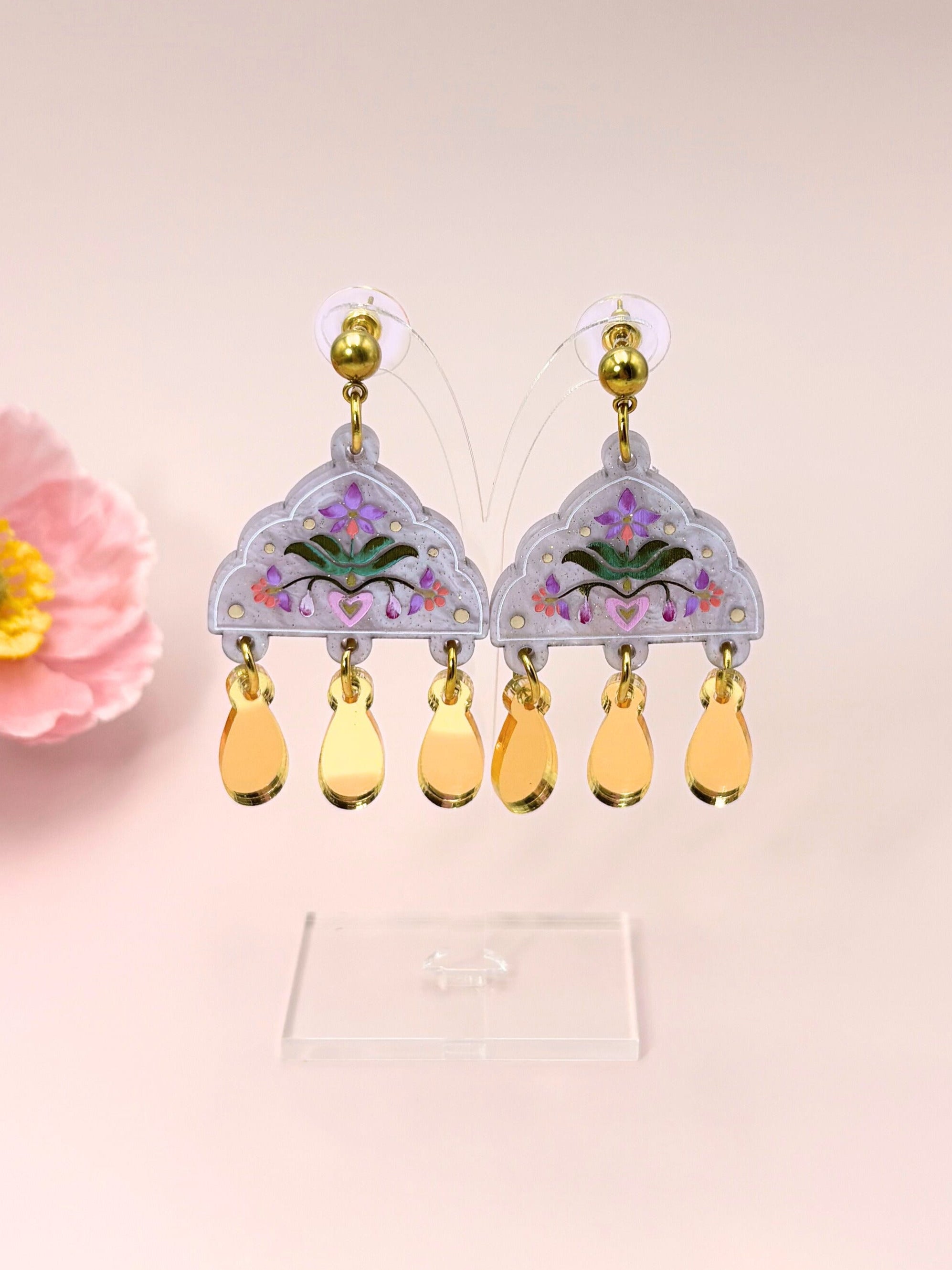 Decorative earrings with floral design and yellow beads on a pink background