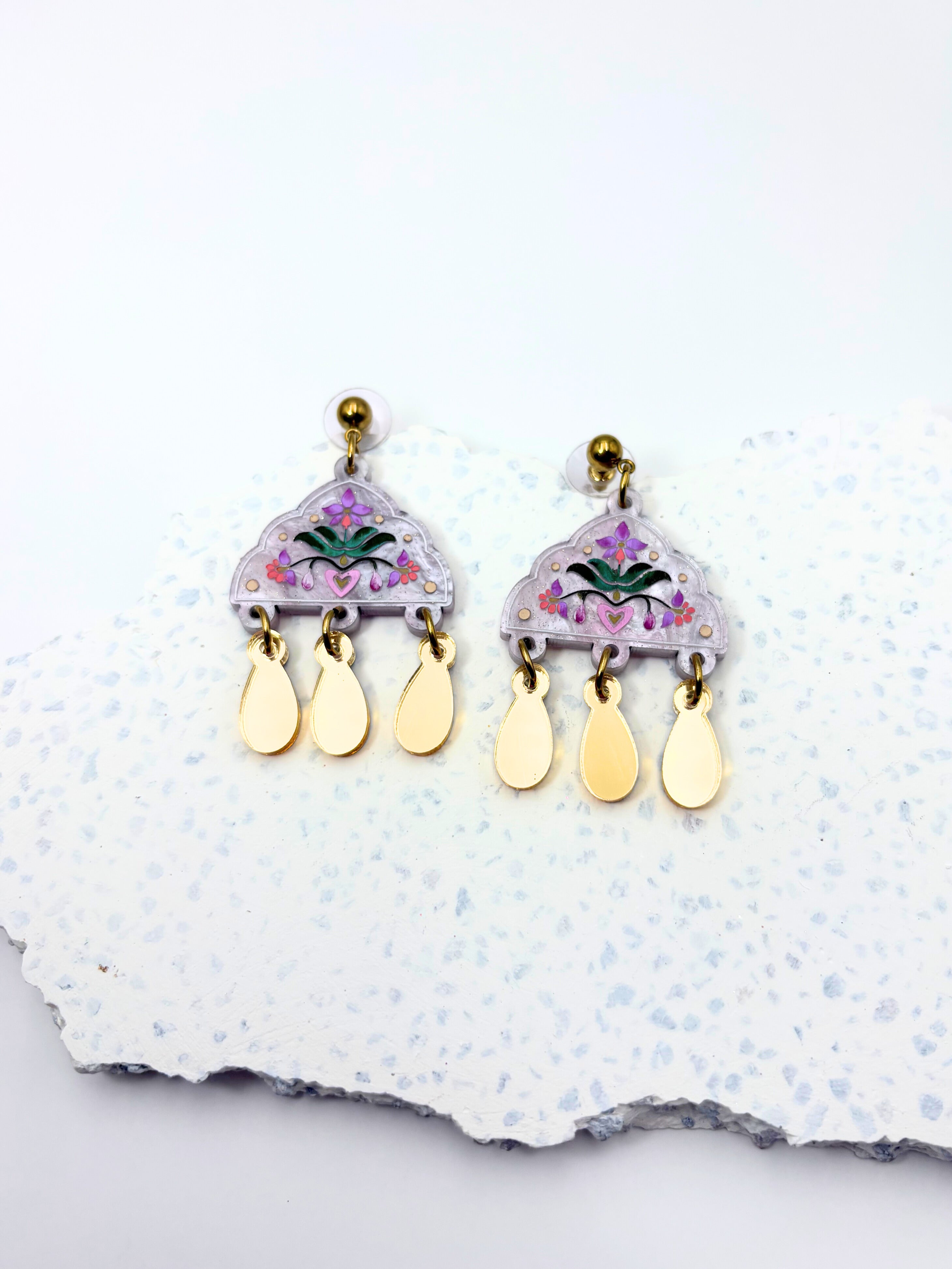 Pair of floral acrylic earrings with gold accents on a textured white surface