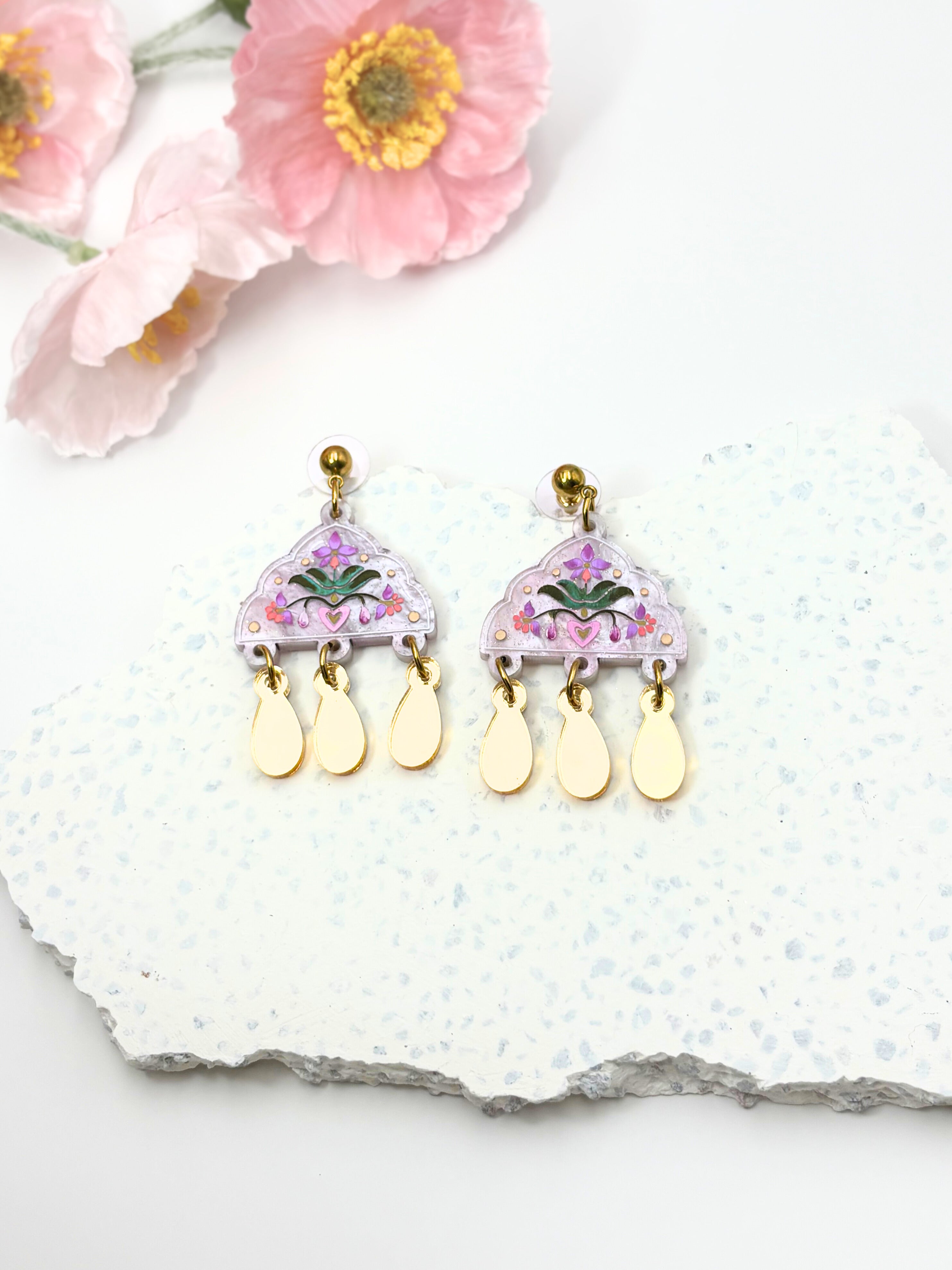 Floral acrylic earrings with teardrop-shaped drops on a white stone surface with pink flowers.