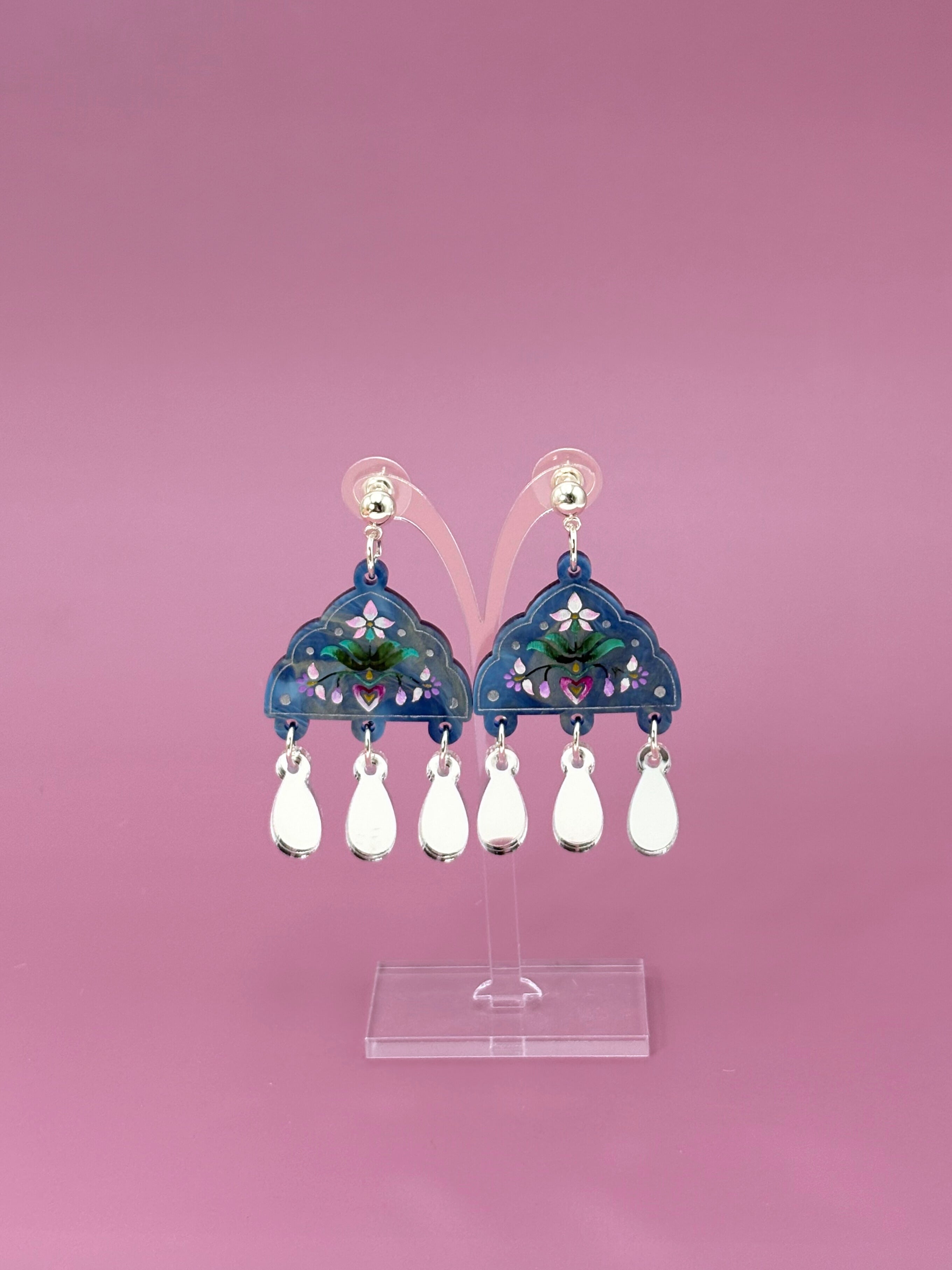 Decorative earrings with teardrop-shaped beads on a pink background