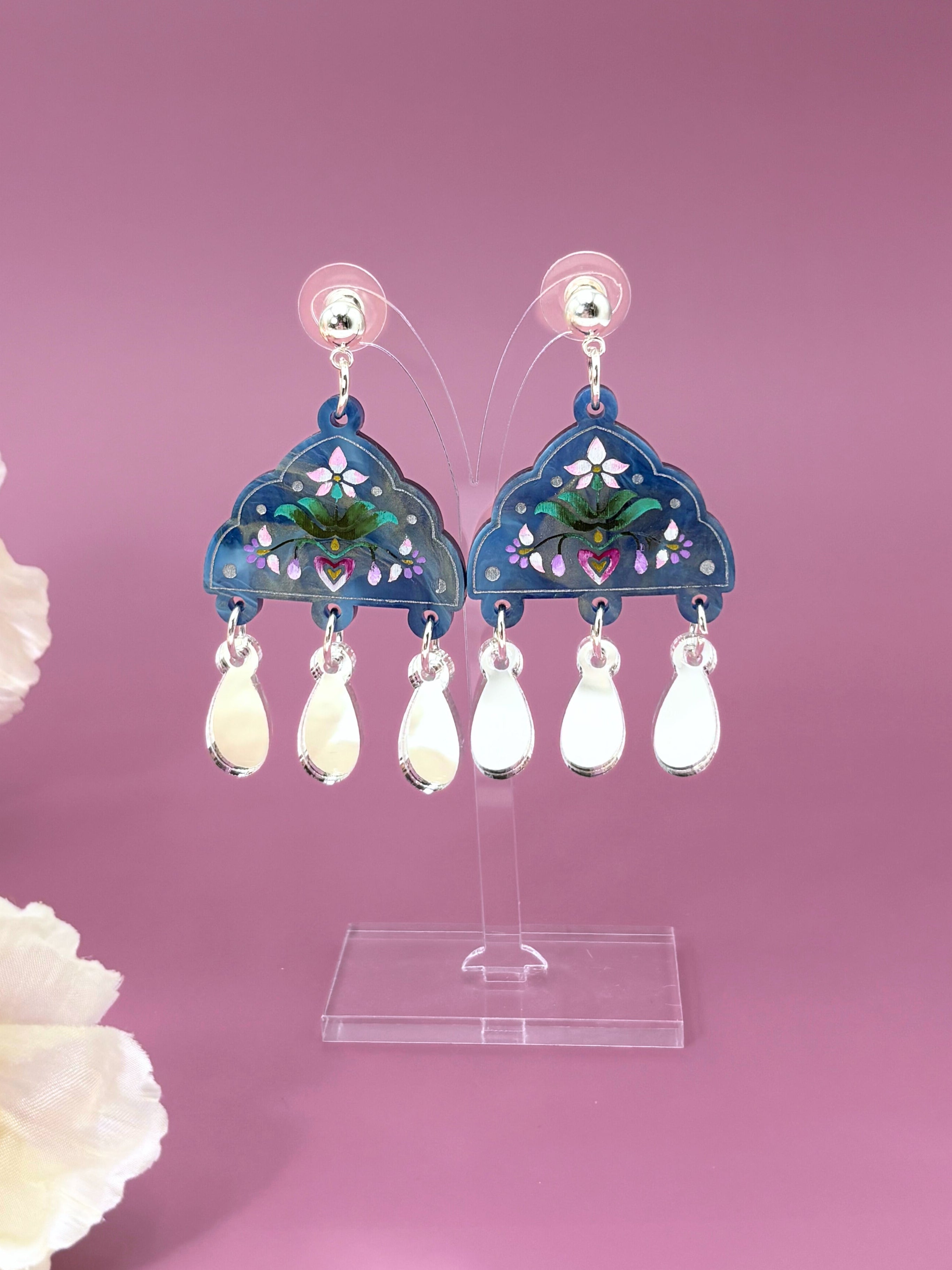 Decorative acrylic earrings on a stand with a pink background