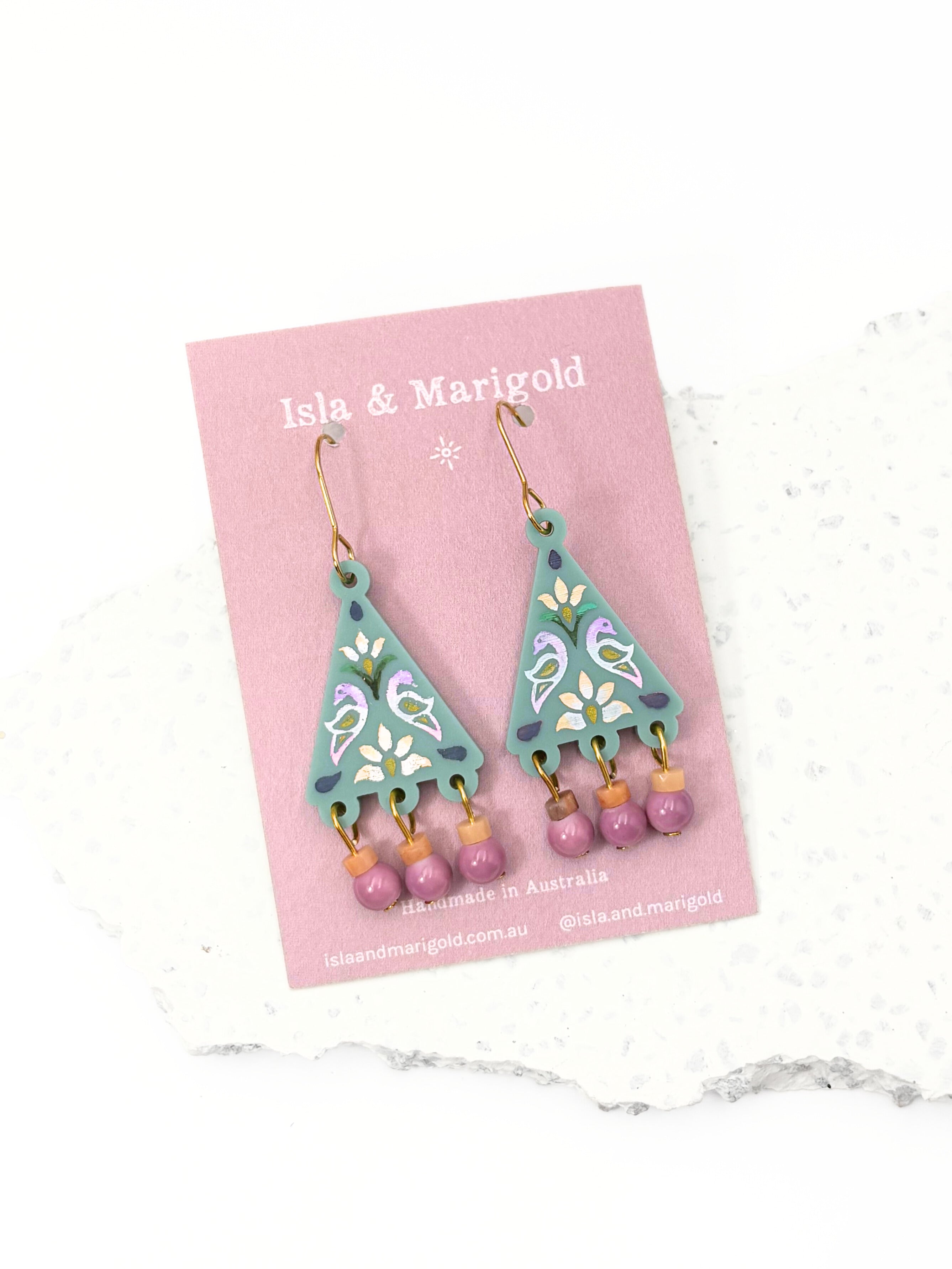Decorative earrings on a pink card with 'Isla & Marigold' branding.