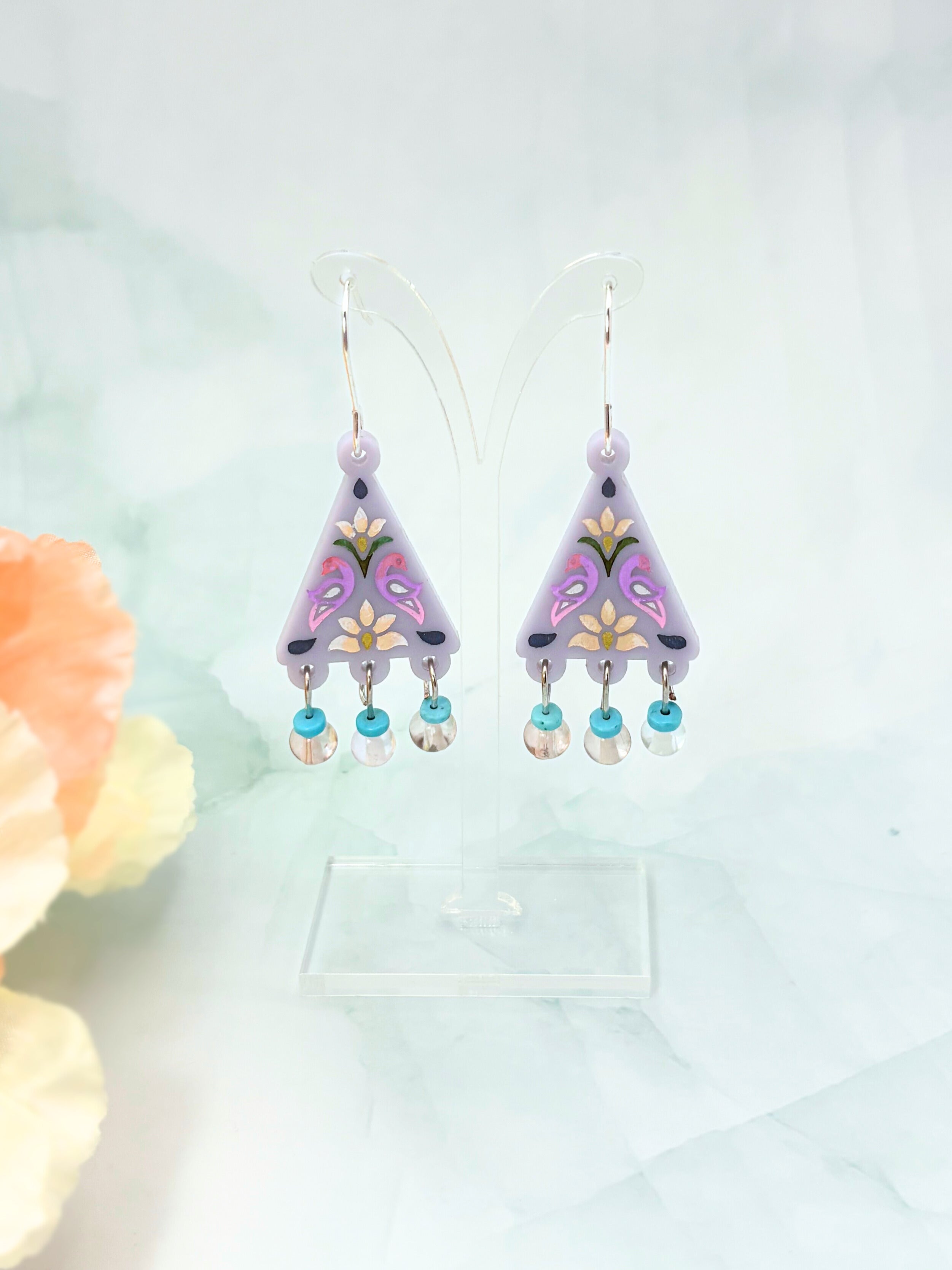 Pair of purple earrings with floral designs and pearl-like beads on a light background