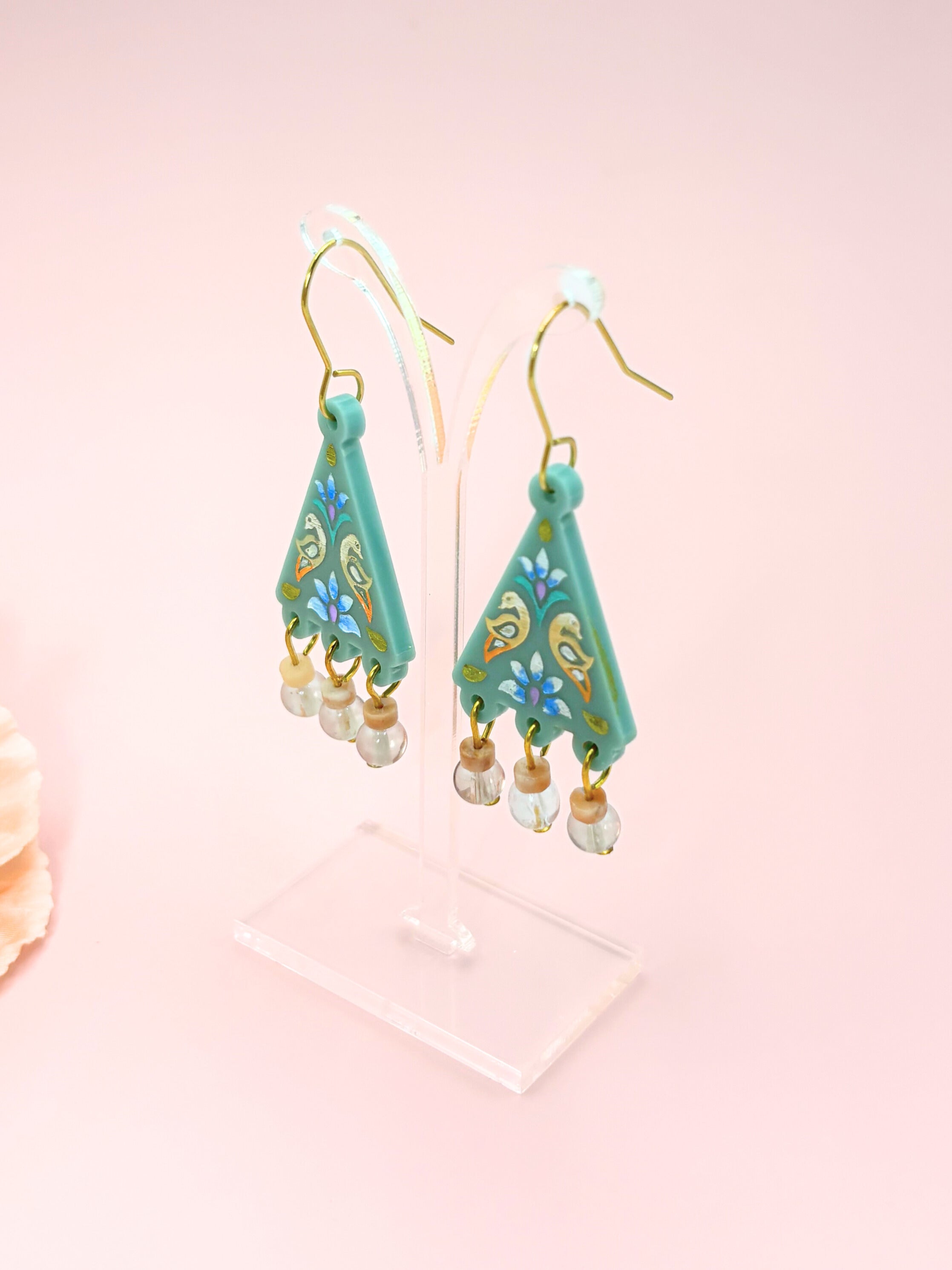 Teal earrings with floral patterns on a pink background