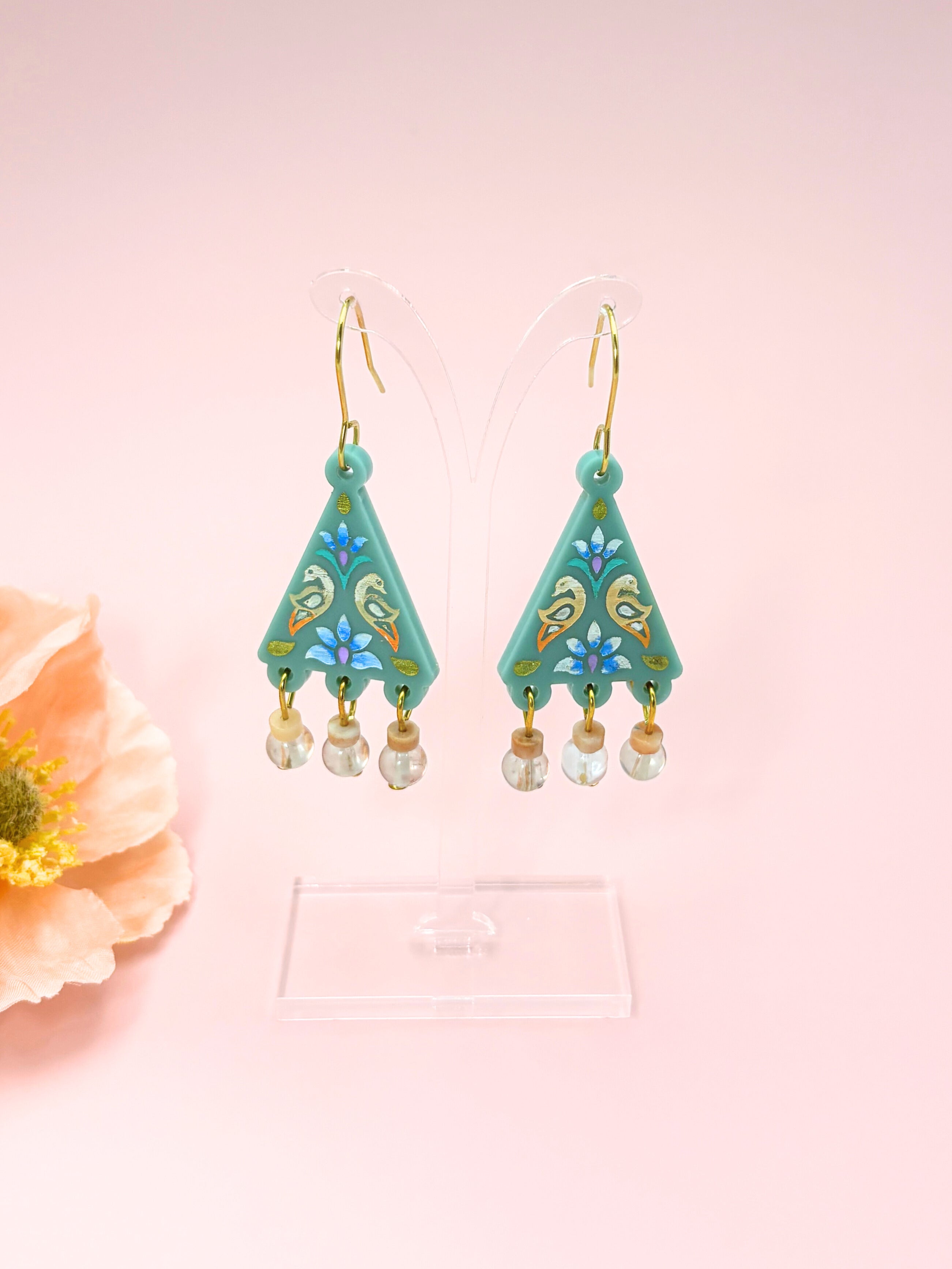 Pair of turquoise earrings with floral designs on a pink background