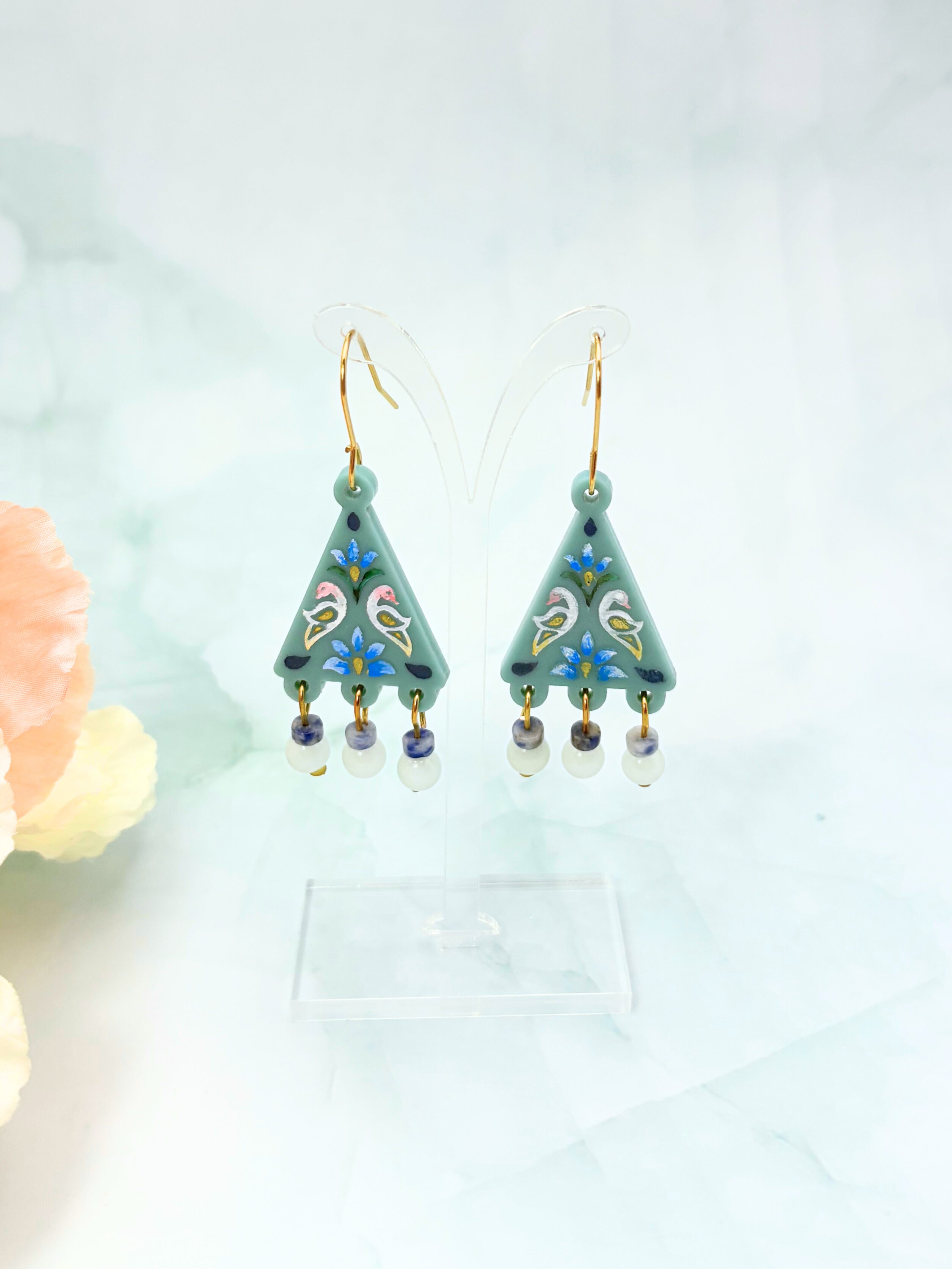 Pair of green earrings with floral designs on a light background