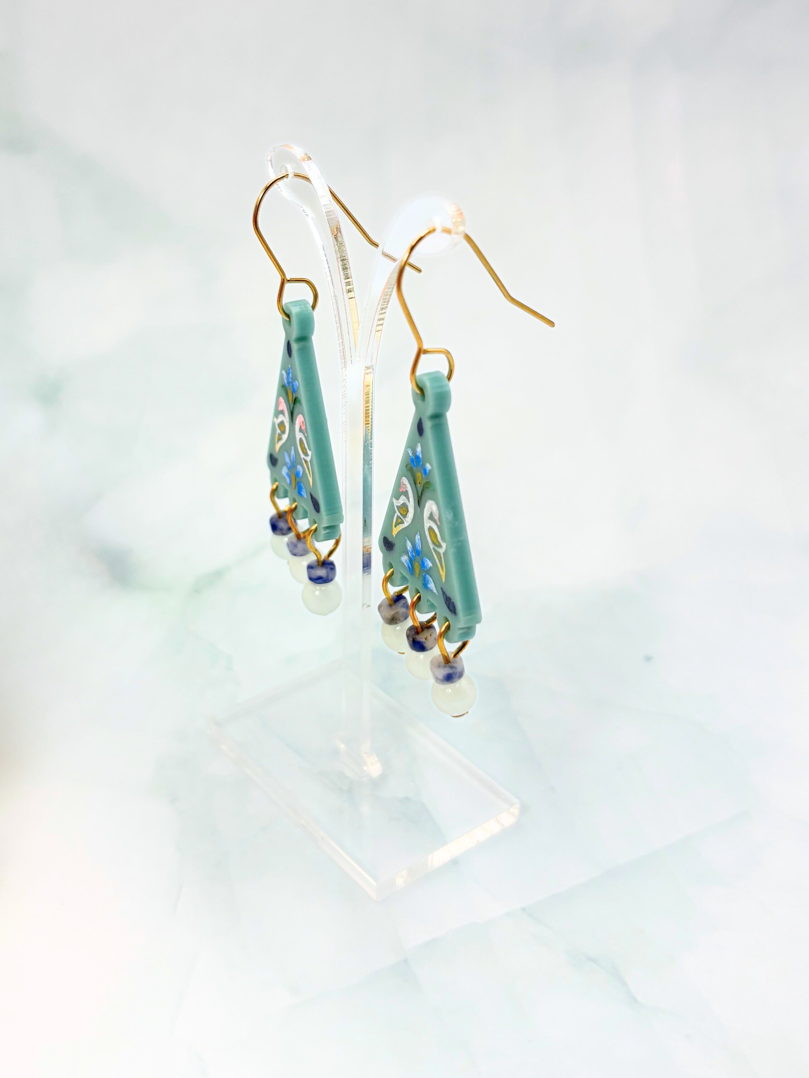 Teal earrings with gold accents on a light gray background