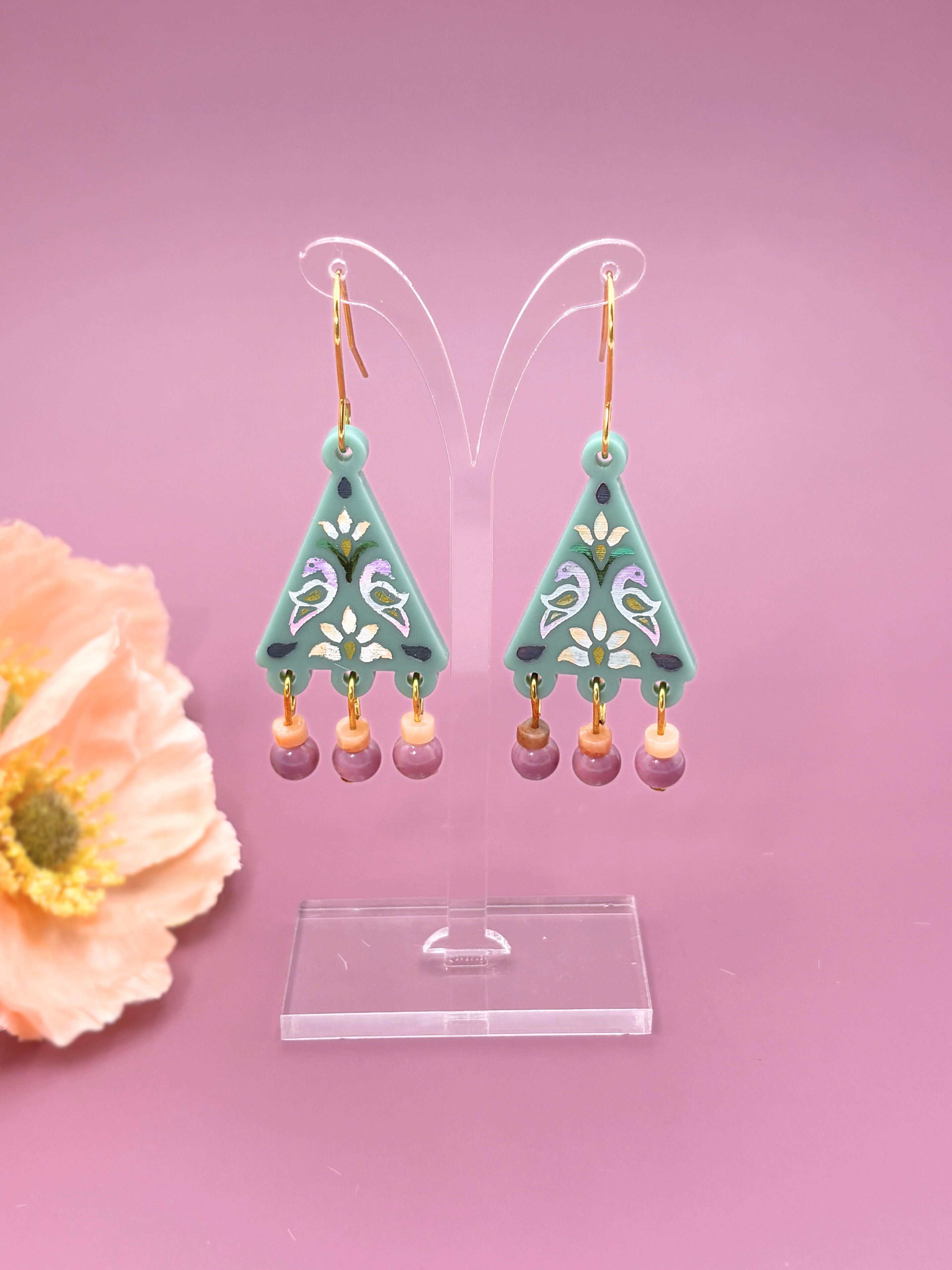 Teal triangle-shaped earrings with pink beads on a pink background