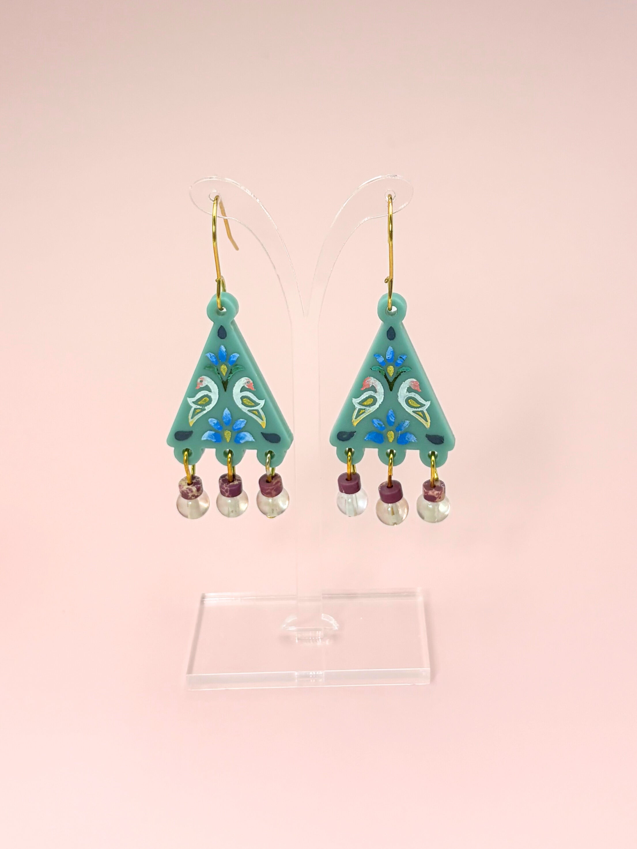 Pair of turquoise earrings with floral designs on a pink background