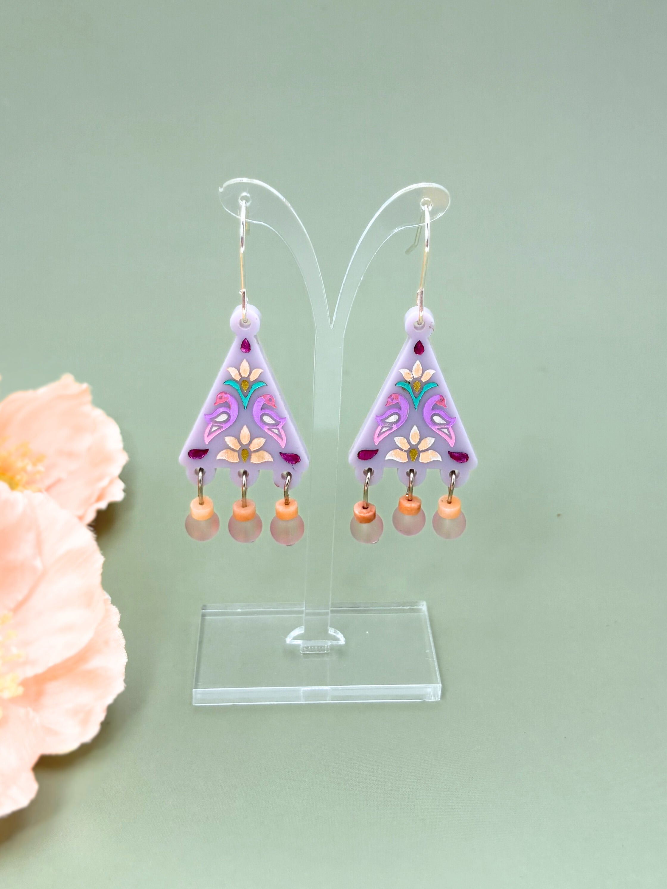 Pair of colorful earrings on a clear stand with a light green background