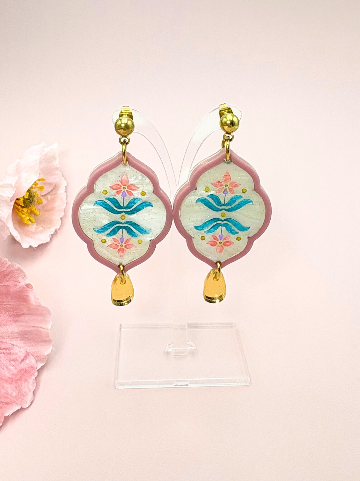 Decorative earrings with floral designs on a pink background