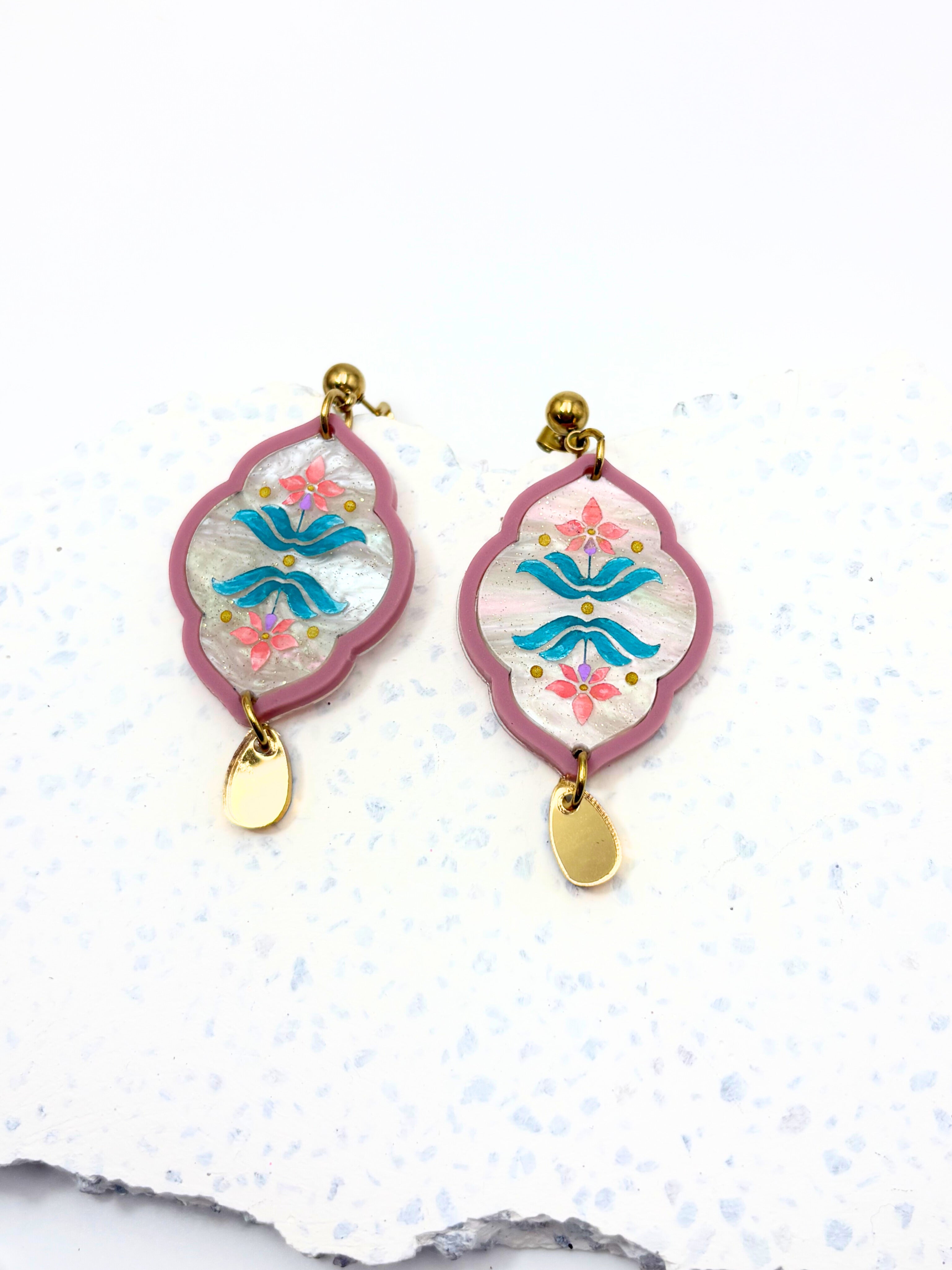 Pair of earrings with floral and abstract designs on a white background