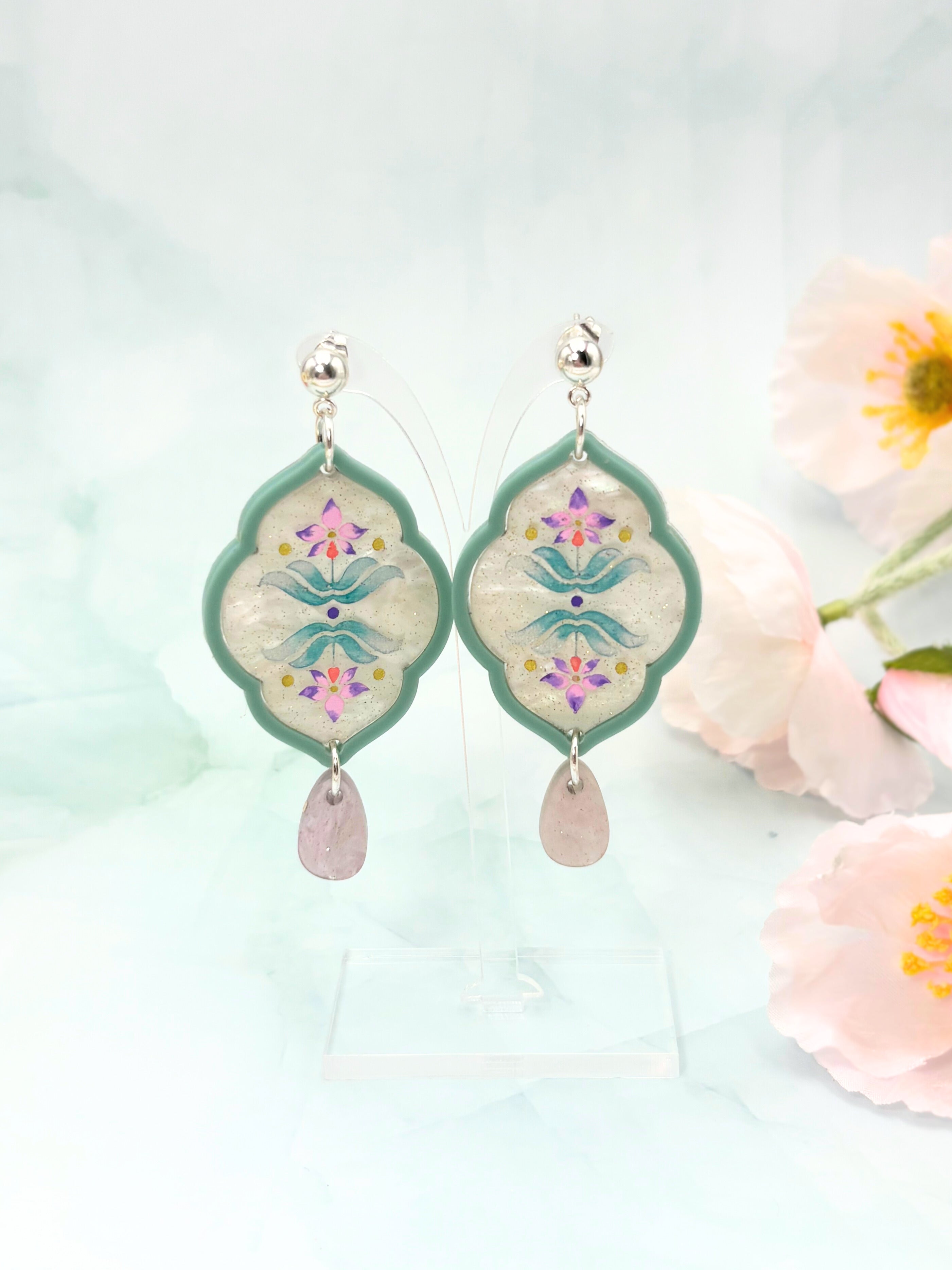Decorative earrings with floral design and pink stones on a light background