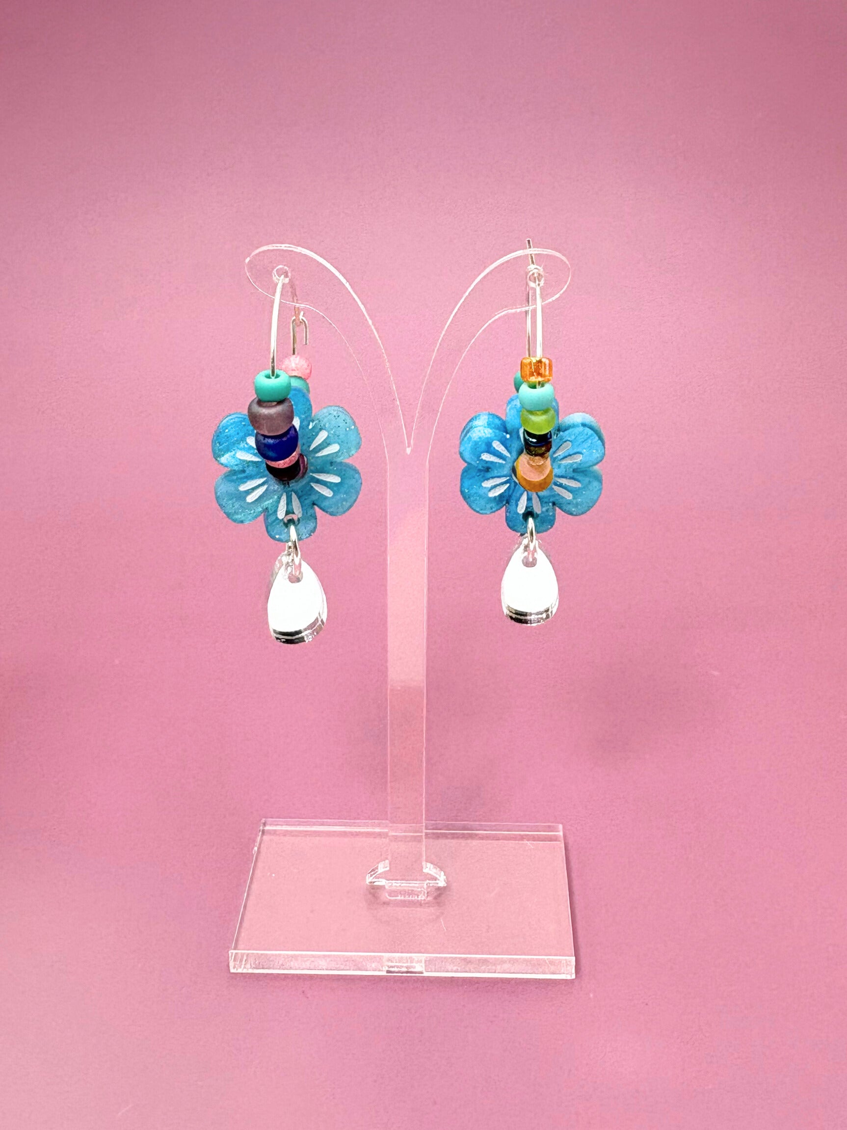 Pair of blue flower-shaped earrings on a pink background