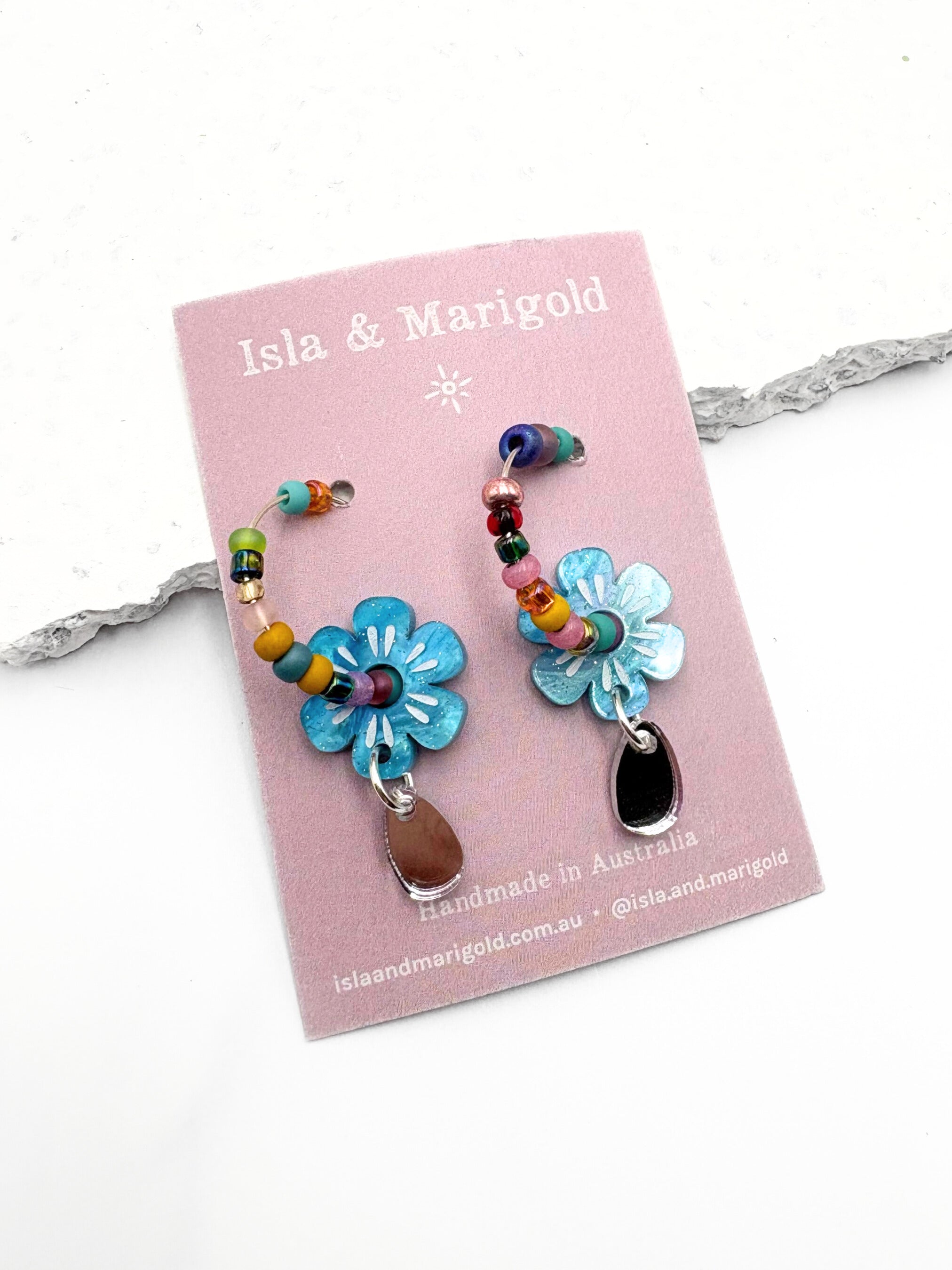 Colorful floral earrings on a pink card with 'Isla & Marigold' branding.