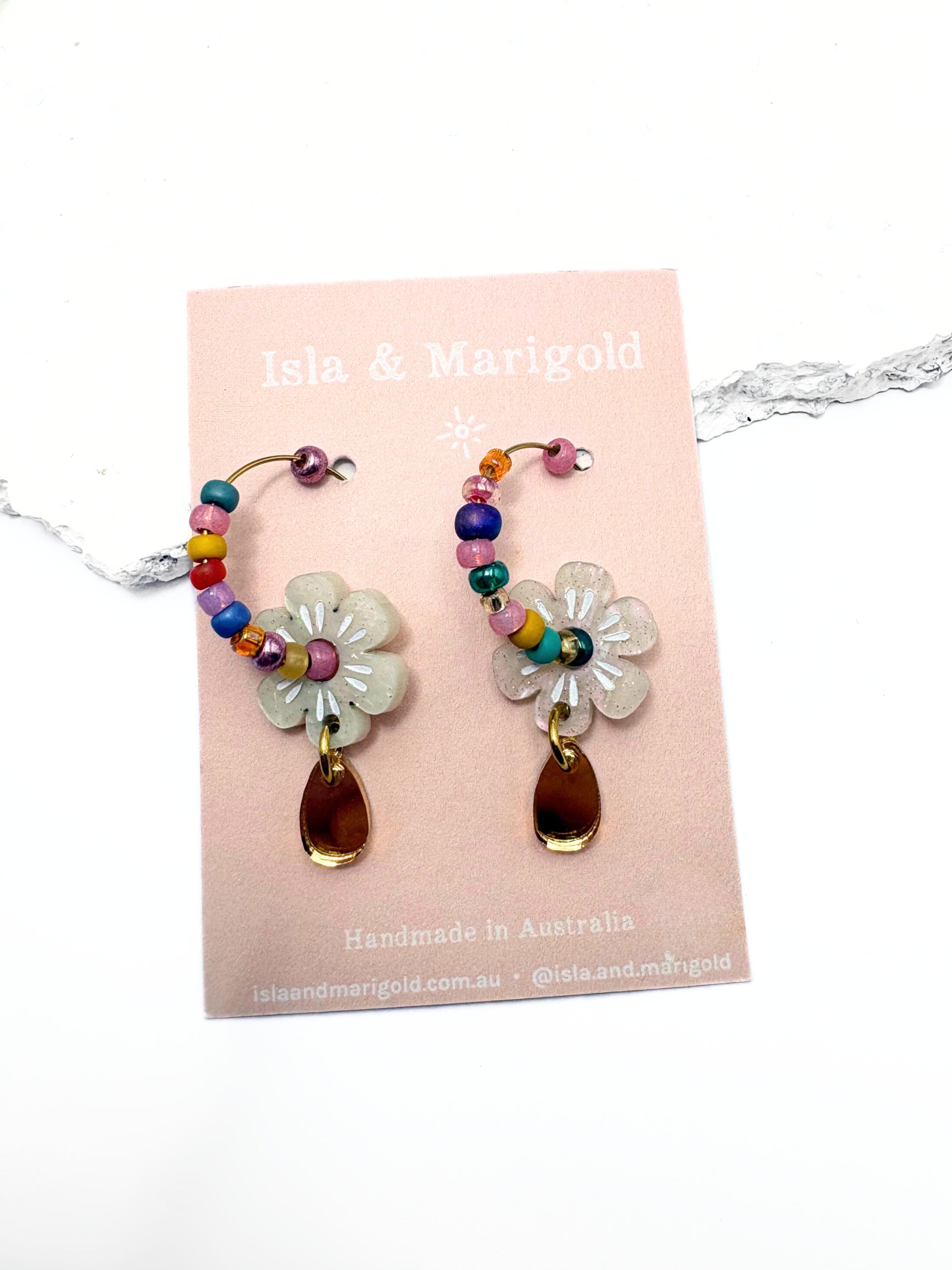 Colorful flower-shaped earrings on a pink card with 'Isla & Marigold' branding.