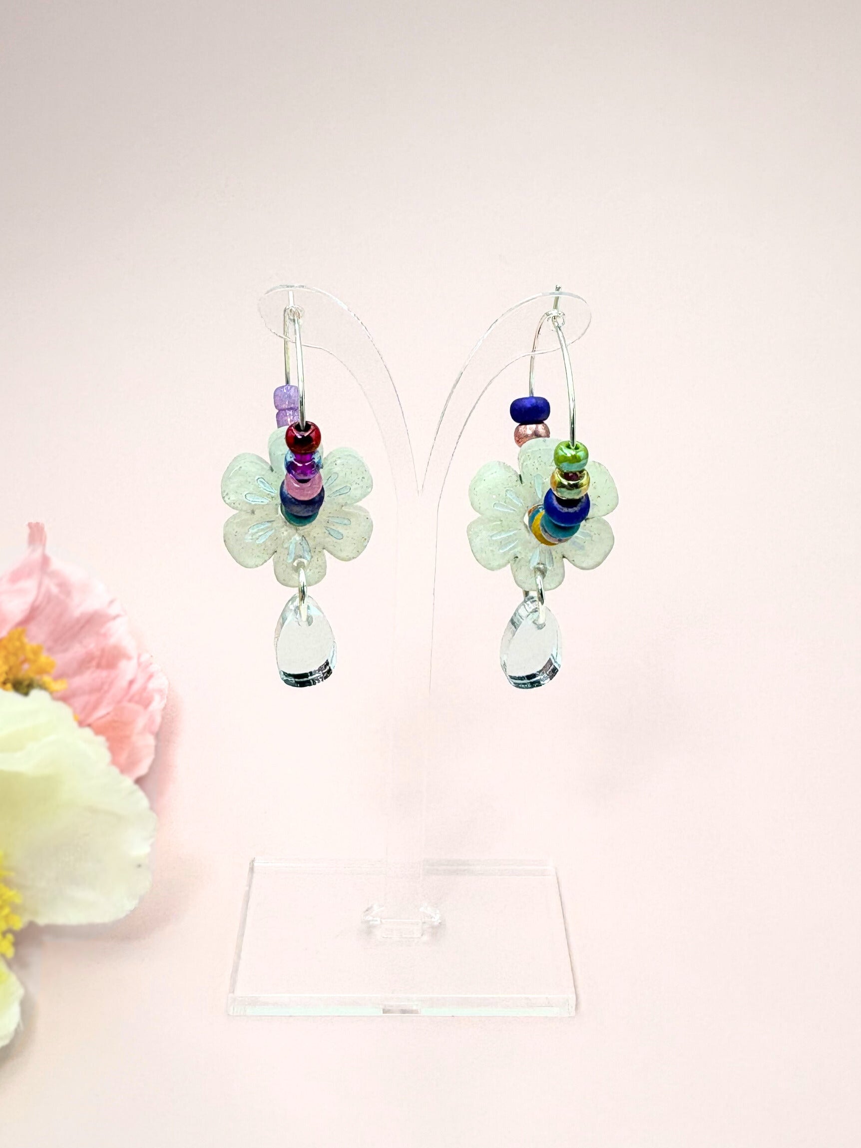 Colorful beaded earrings on a pink background with flowers.