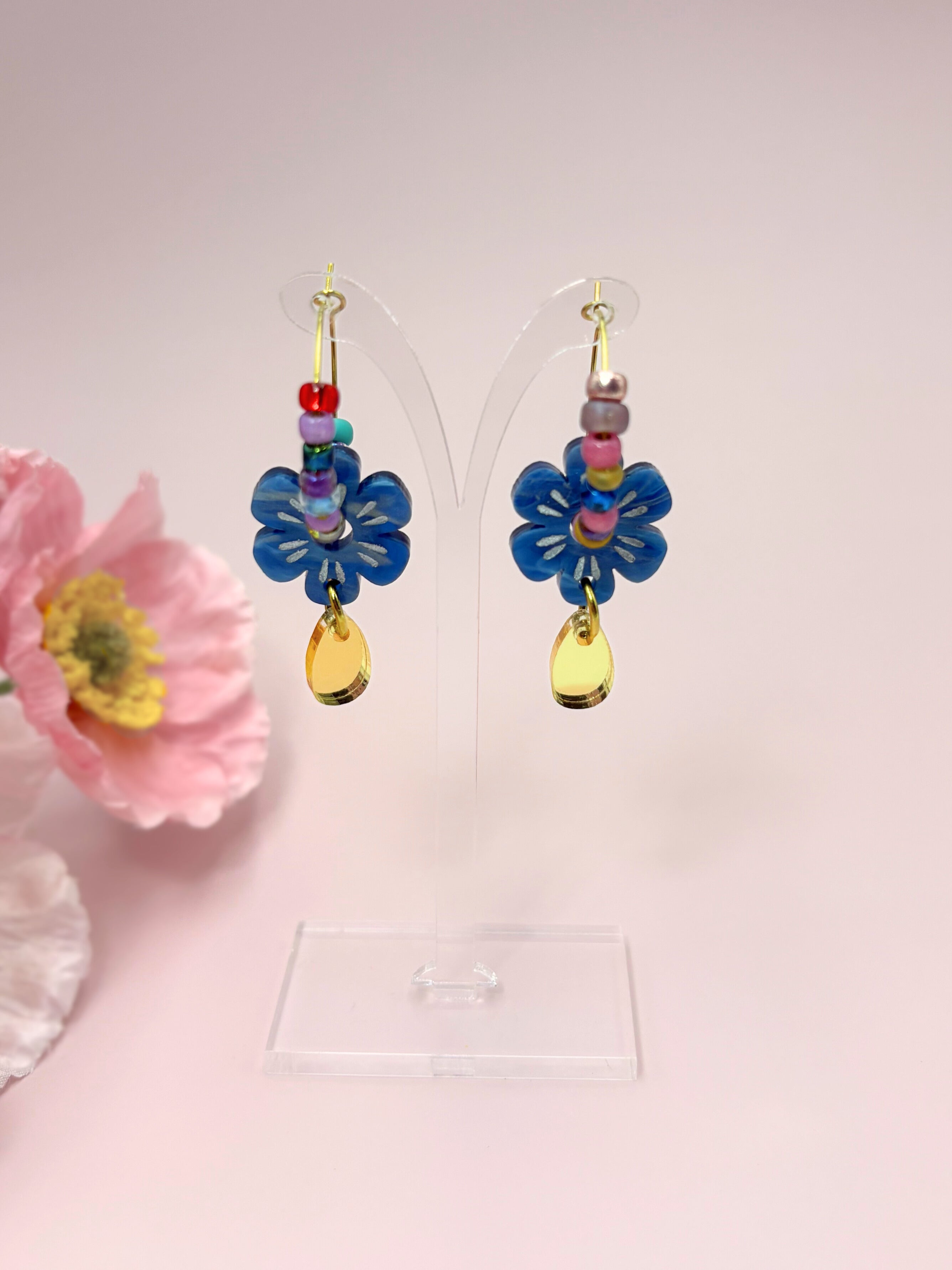 Colorful flower-shaped earrings with beads on a pink background