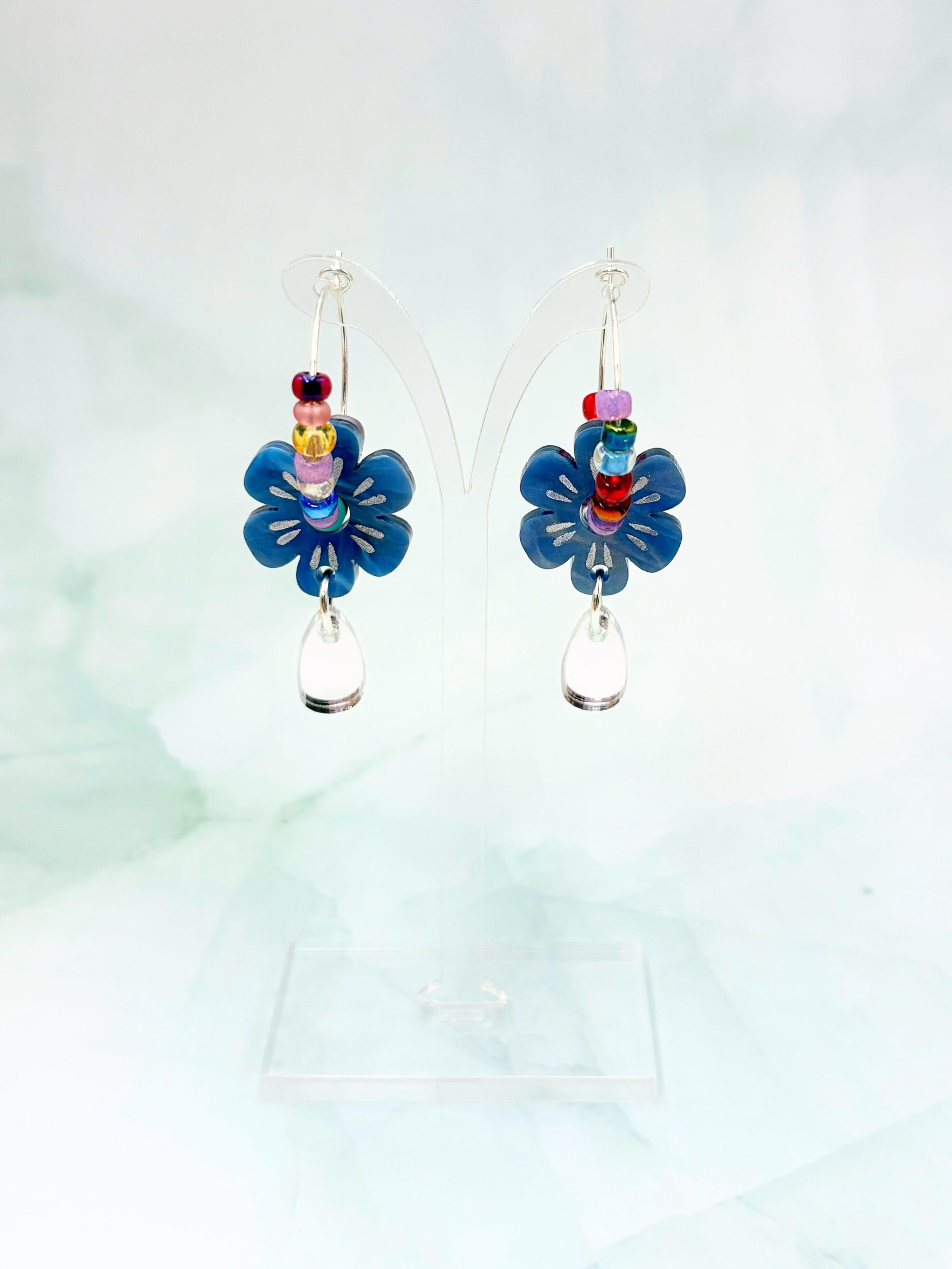 Pair of blue flower-shaped earrings with colorful centers on a light green background