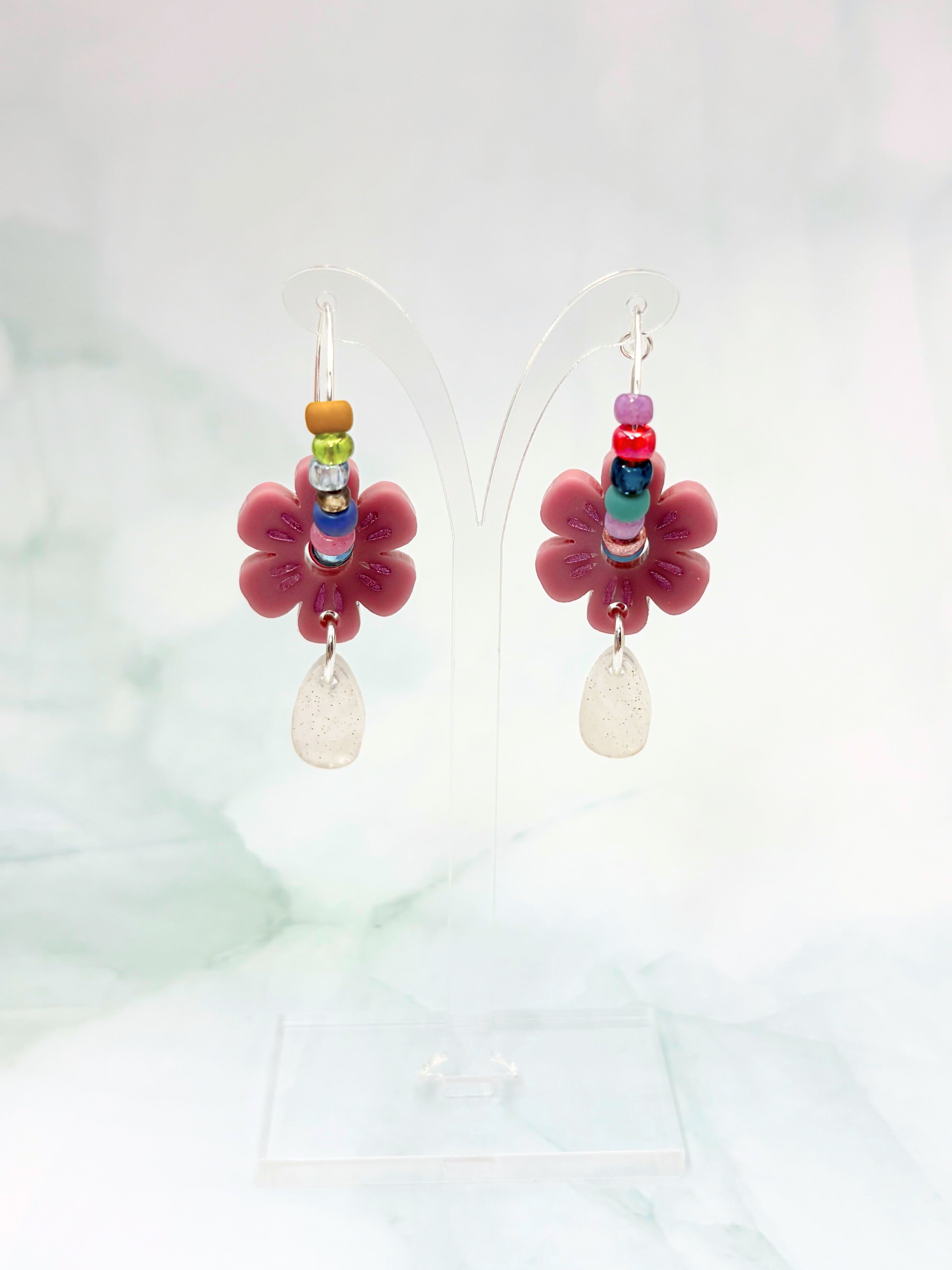 Flower-shaped earrings with colorful beads and pink flowers on a light background