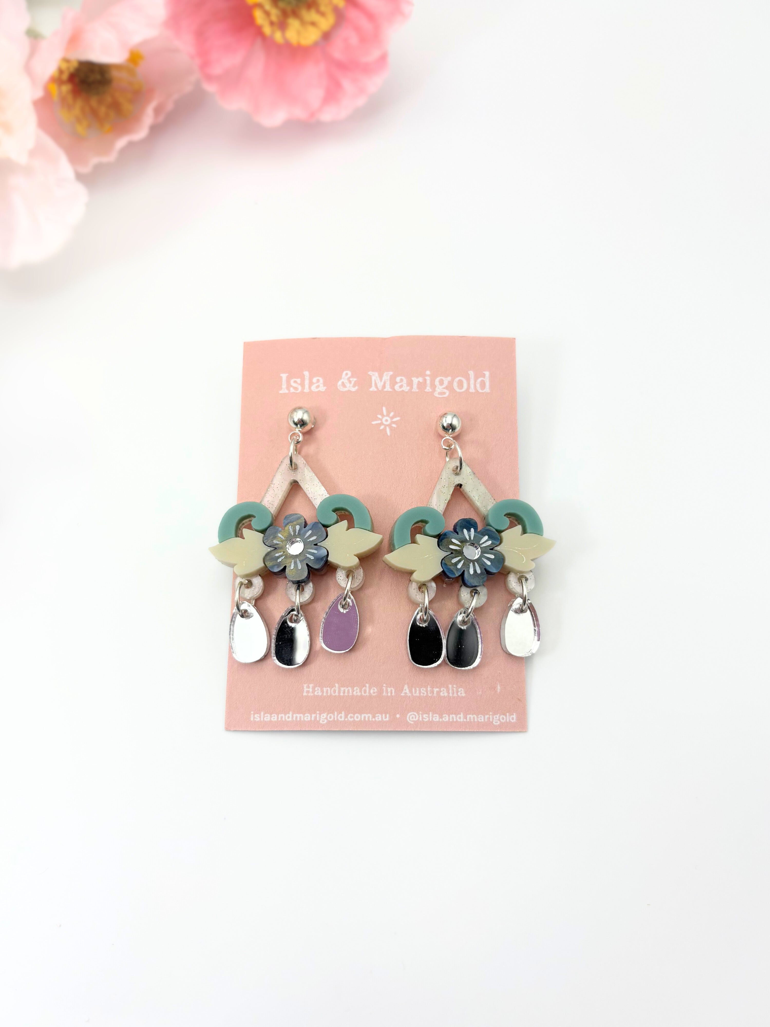 Pair of earrings on a pink card with floral decorations, set against a white background.