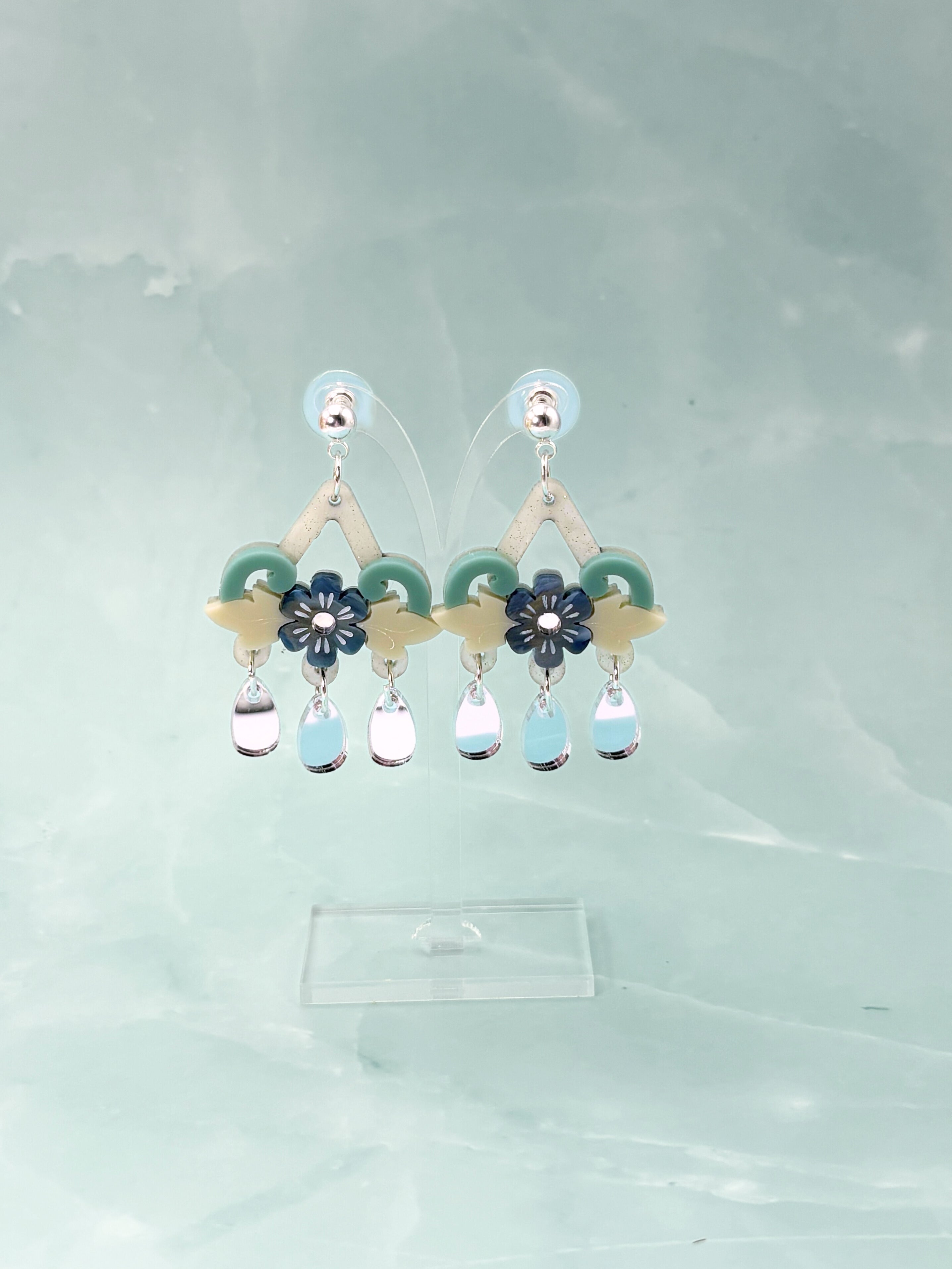 Pair of acrylic and stainless steel earrings with floral designs and colorful beads on a light gray background