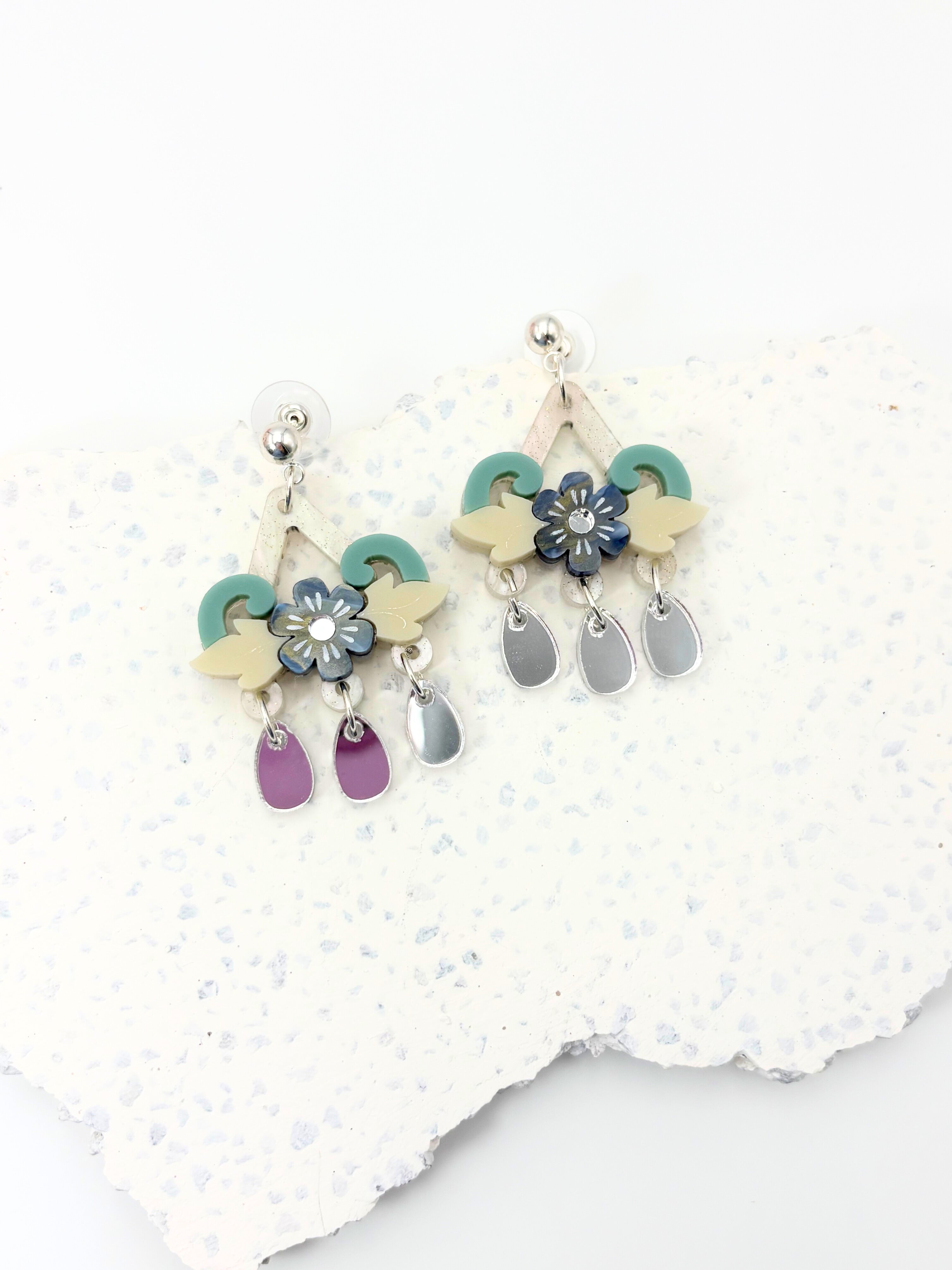 Colorful floral acrylic and silver earrings on a textured white surface