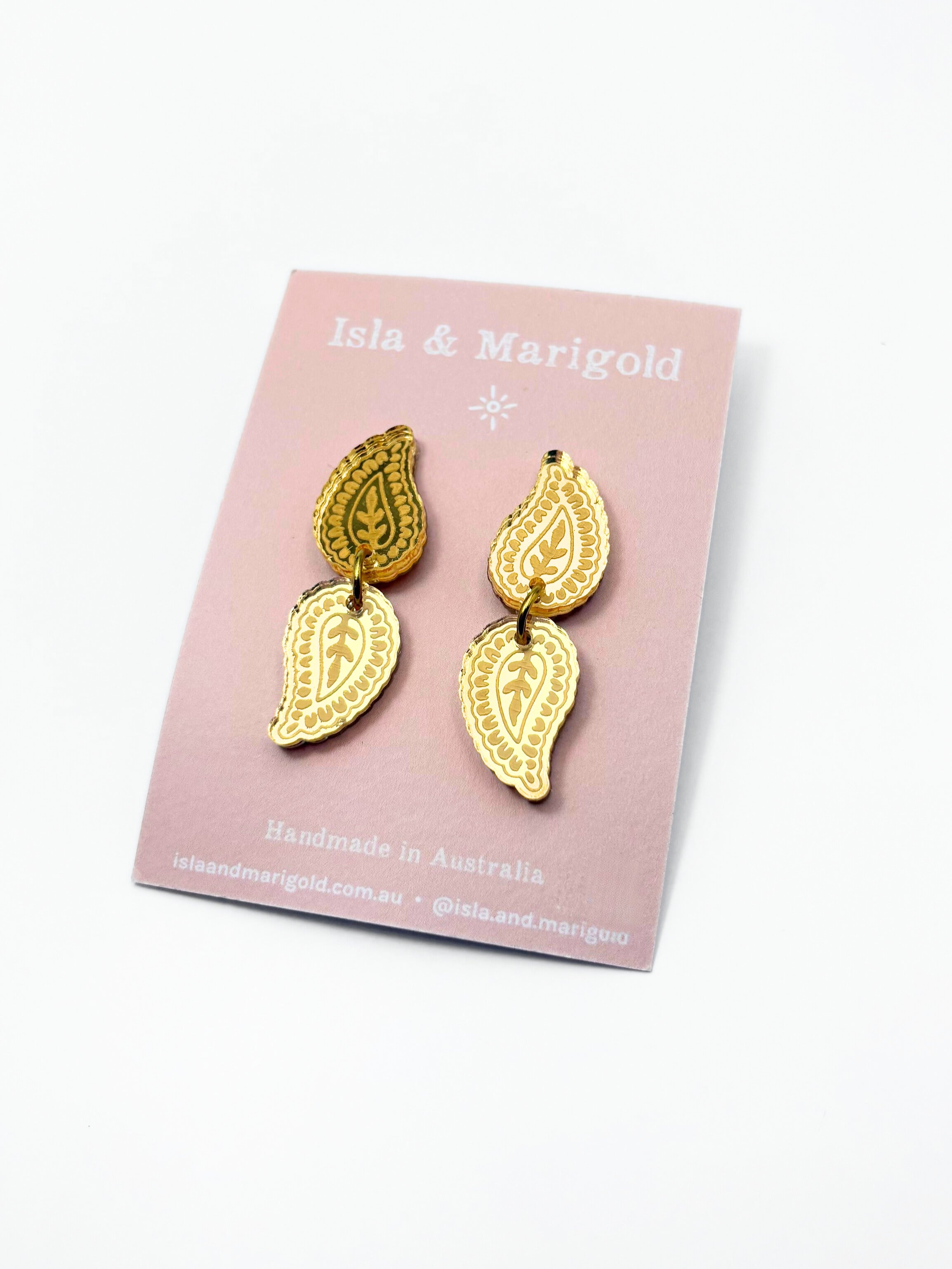 Gold leaf-shaped earrings on a pink card with 'Isla & Marigold' branding.