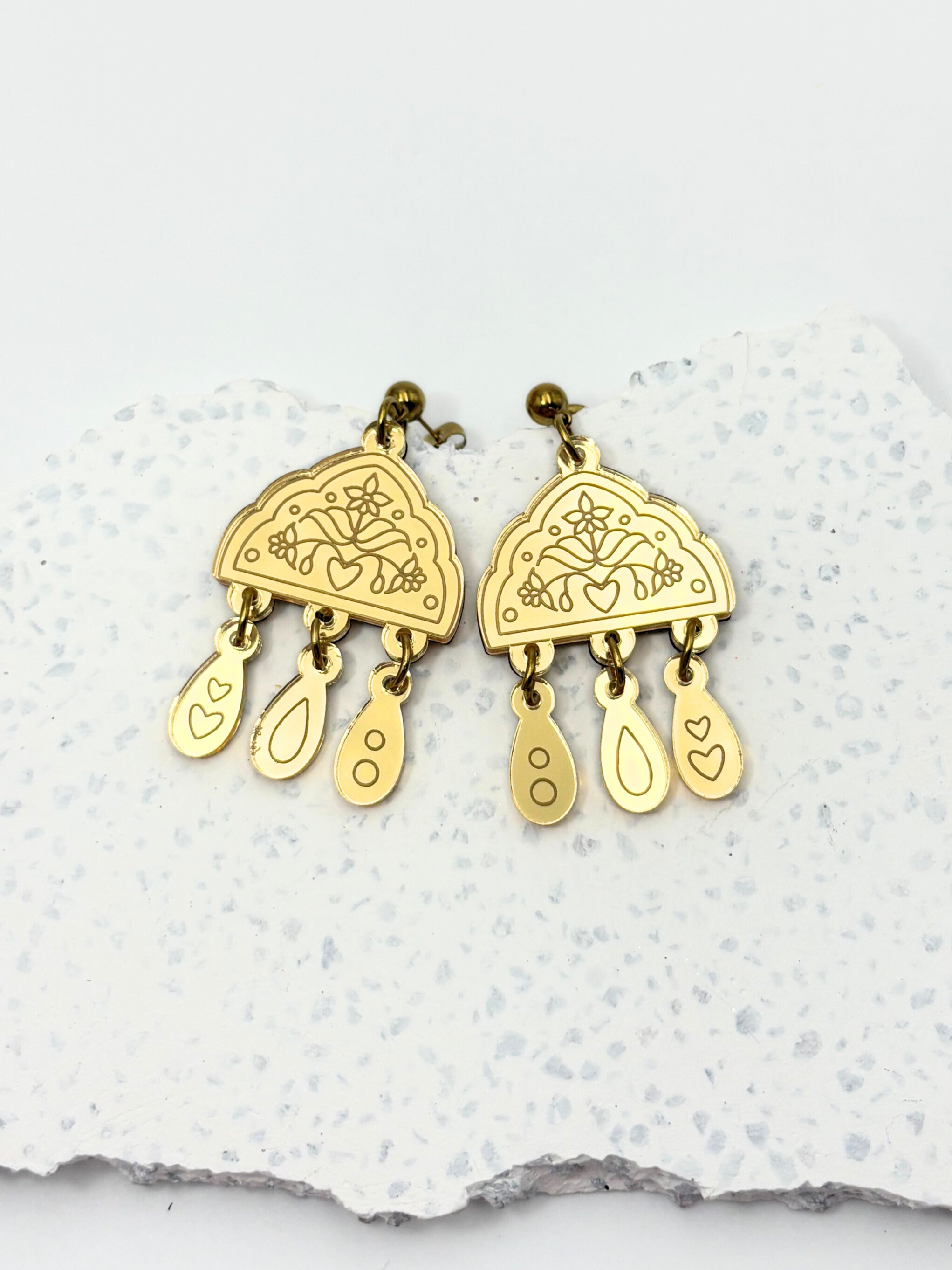 Gold earrings with intricate designs on a textured white surface