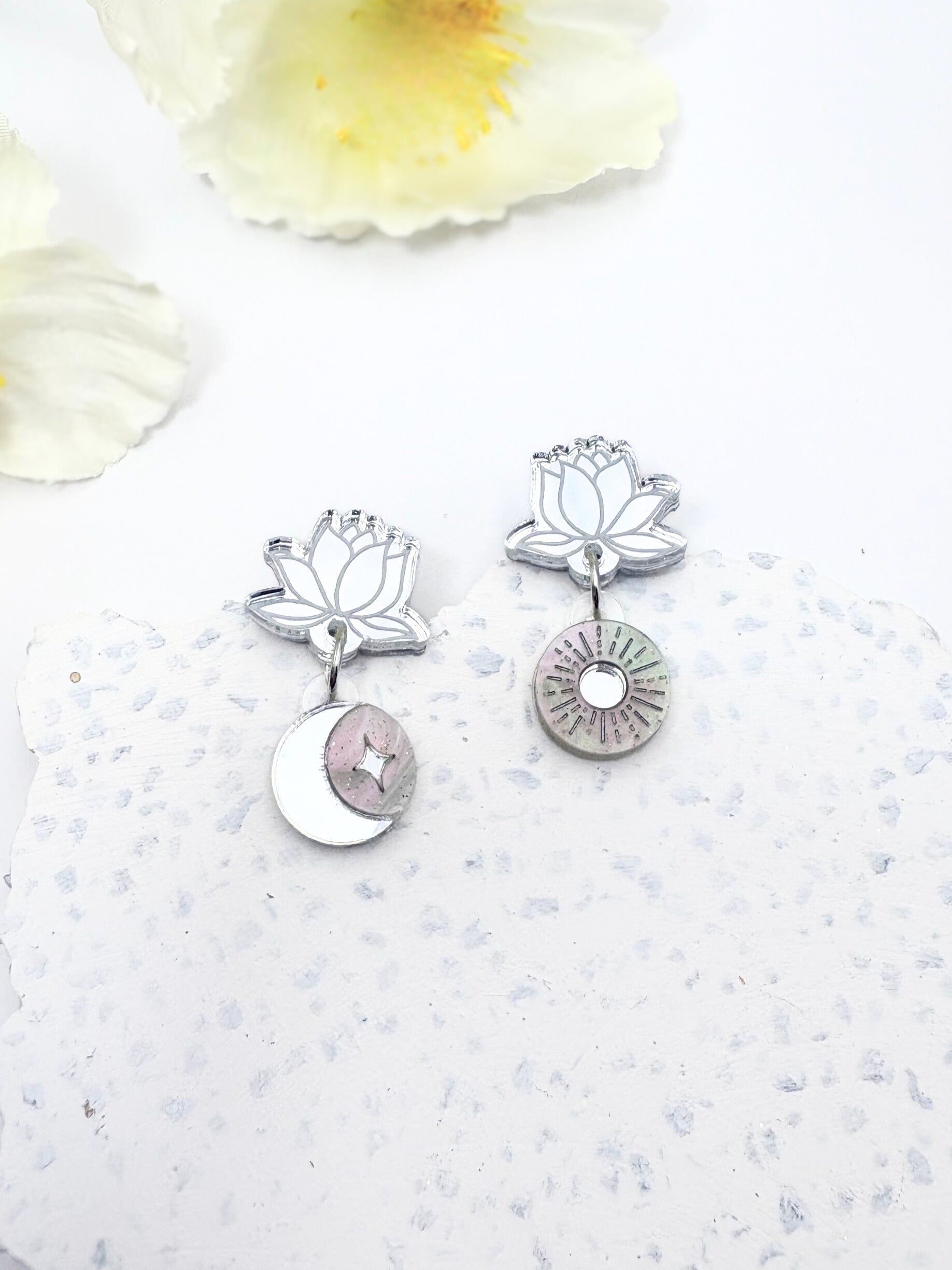 Silver lotus flower earrings on a textured white surface with floral elements.