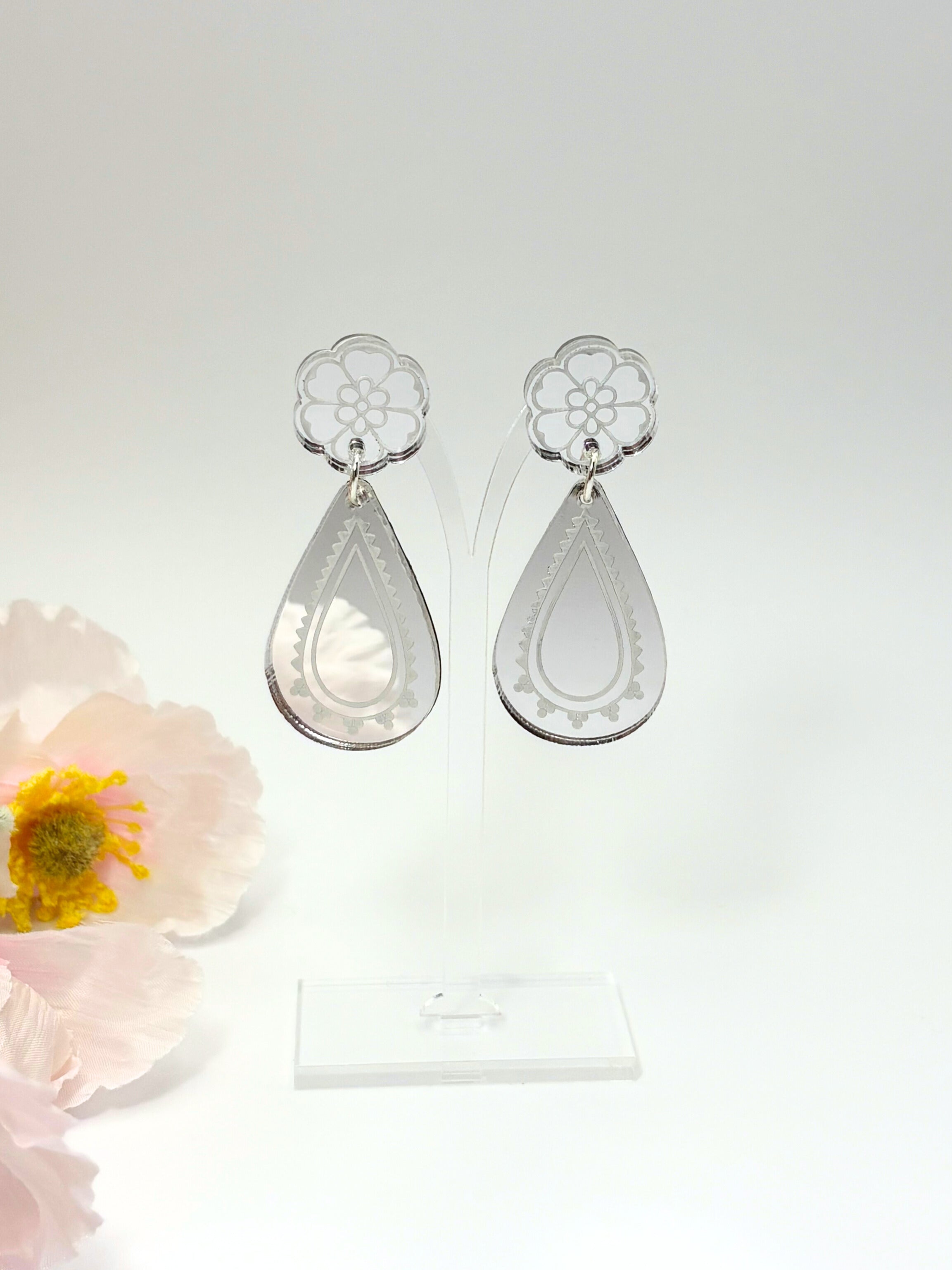 Silver teardrop earrings with floral designs on a white background