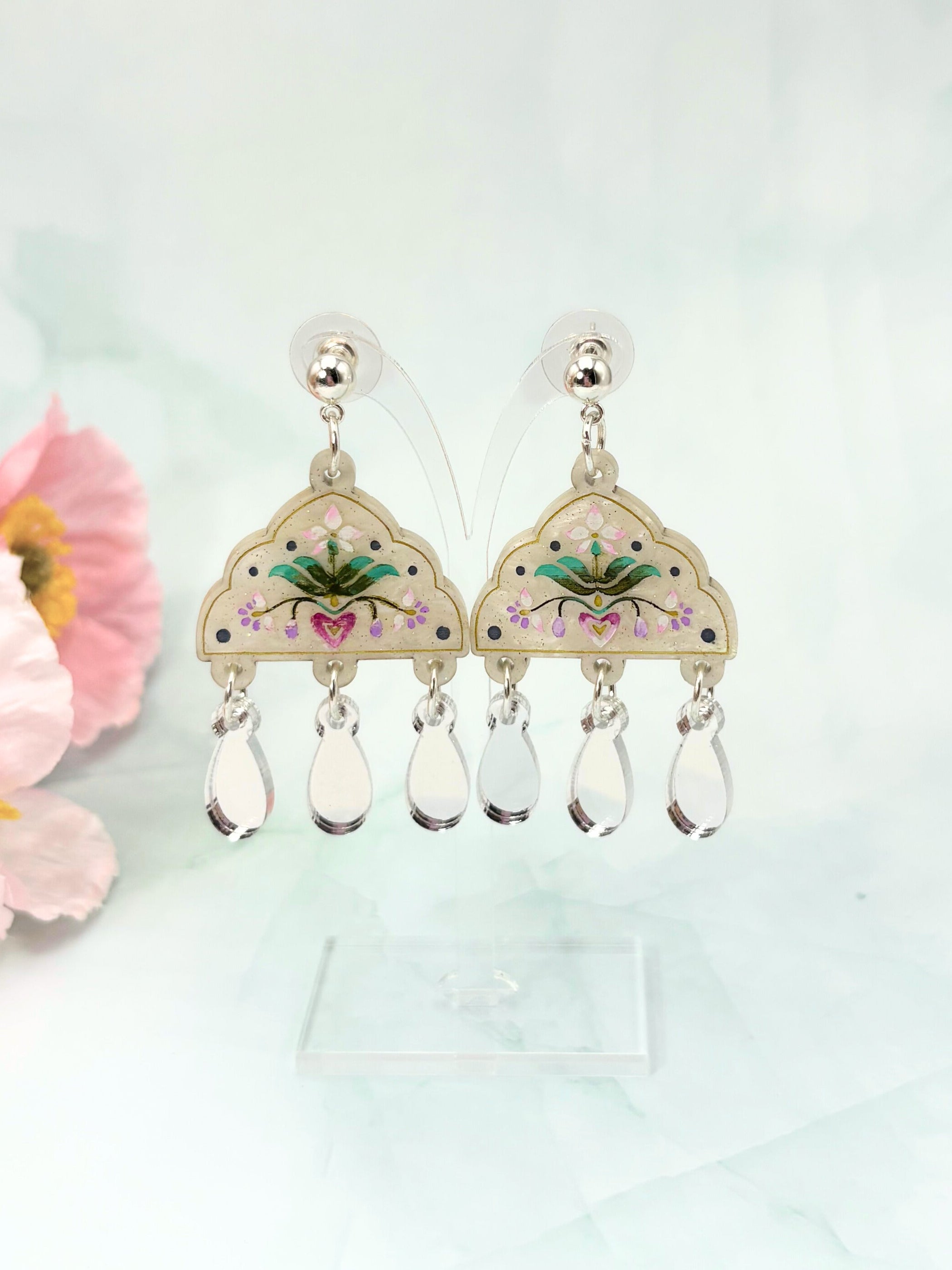 Decorative earrings with floral design and teardrop-shaped elements on a light background.