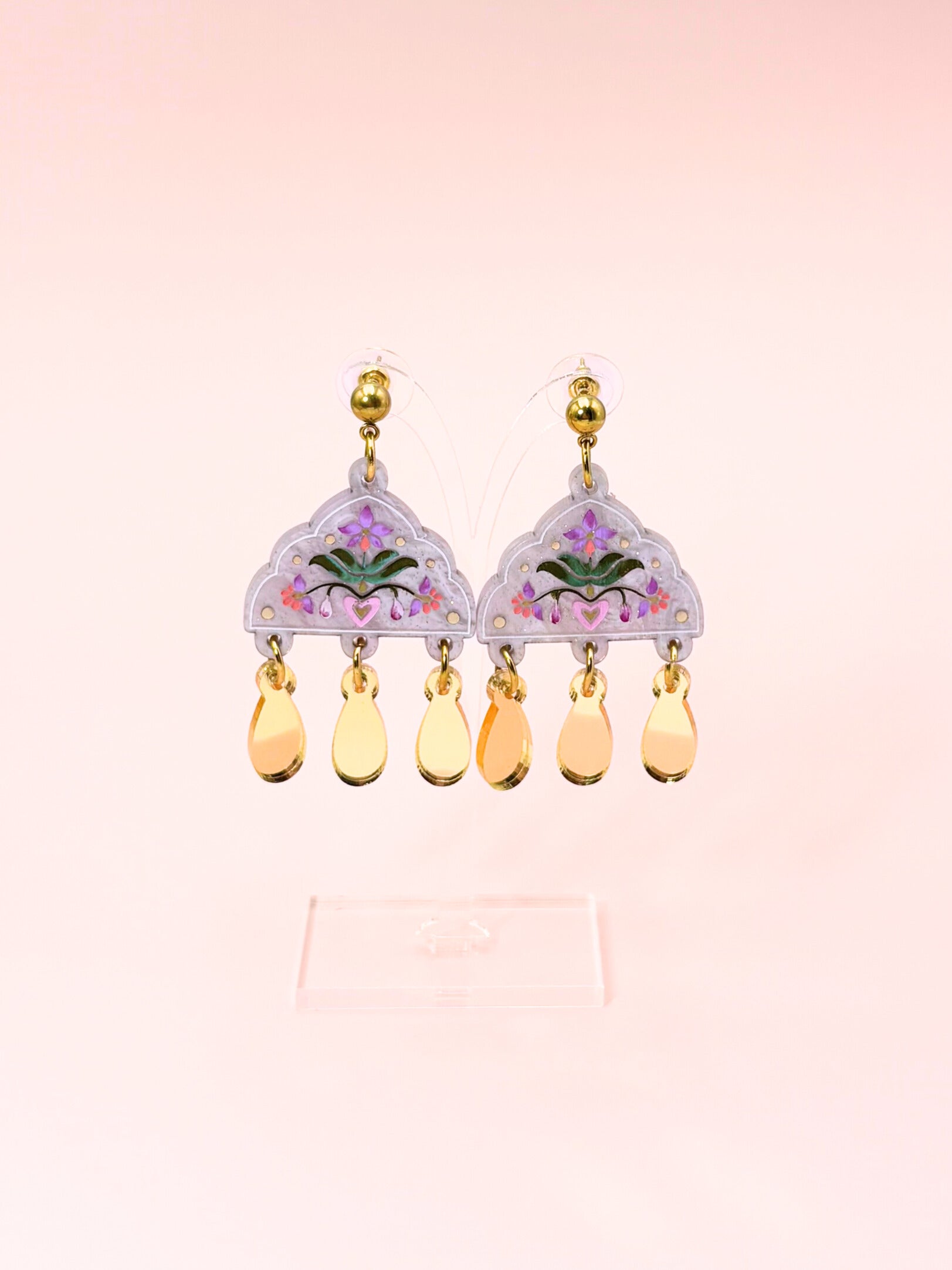 Pair of earrings with floral design and teardrop-shaped beads on a light pink background