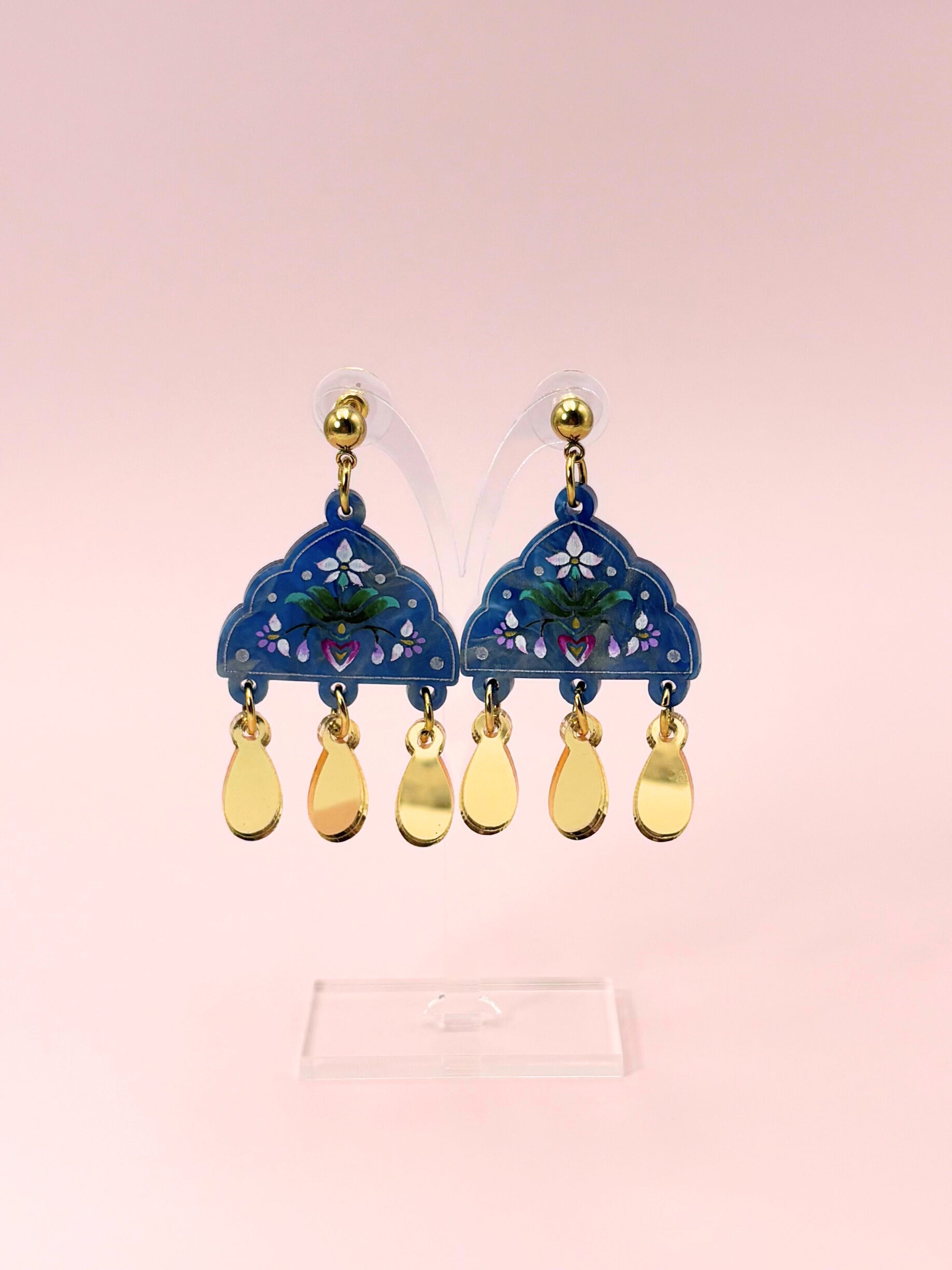 Pair of blue earrings with gold accents on a pink background