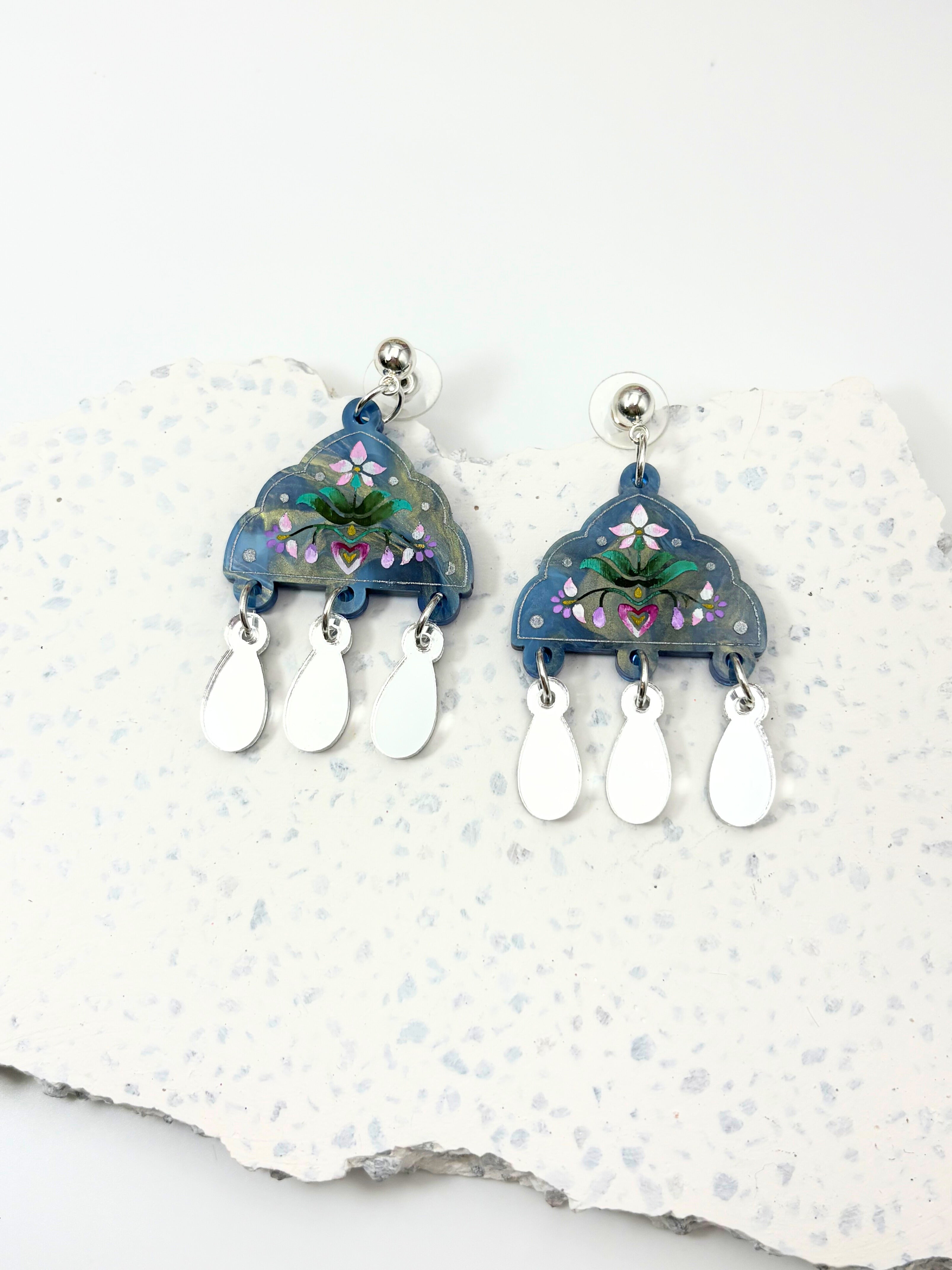 Pair of blue acrylic earrings with floral design on a white stone background