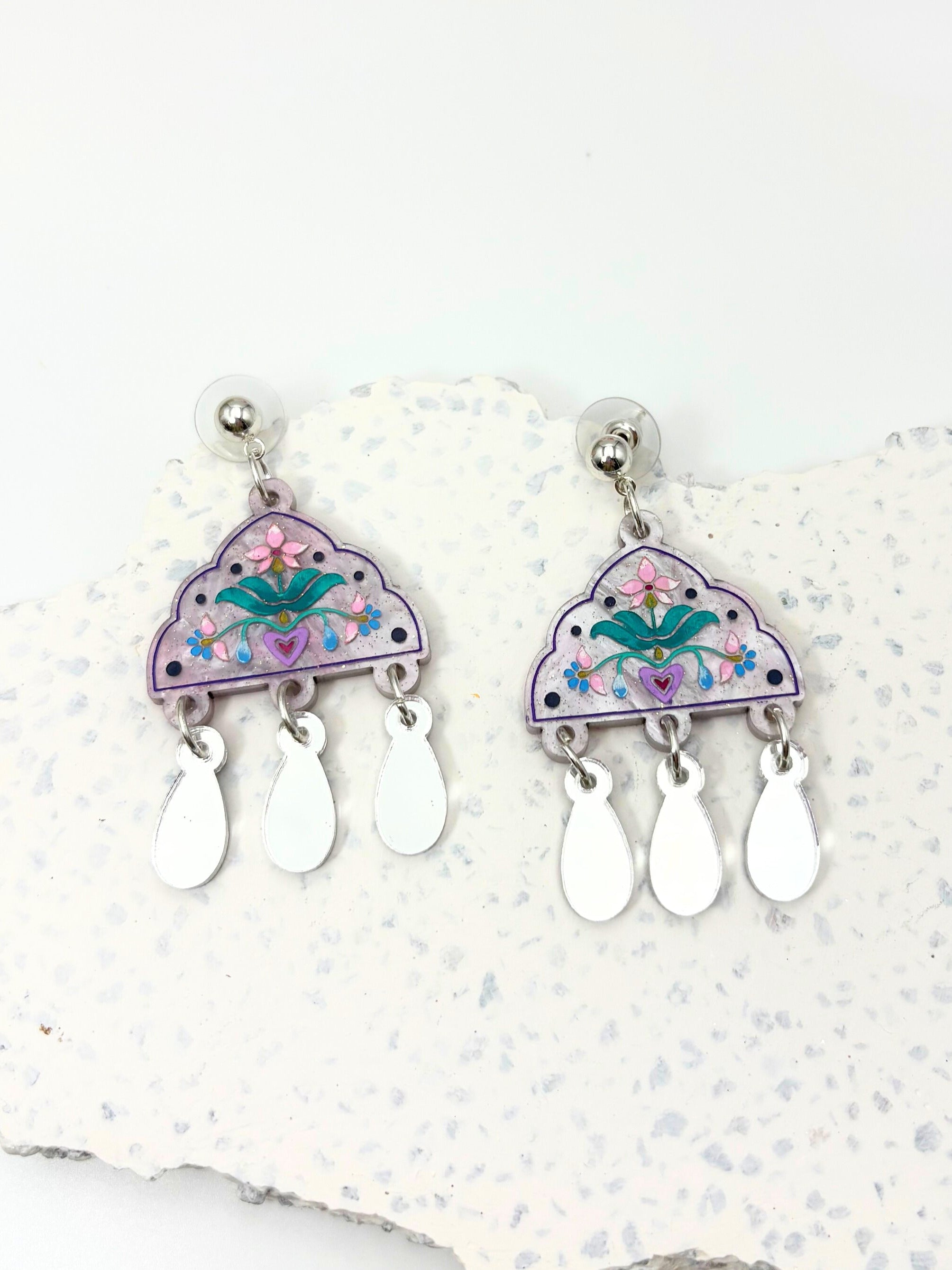 Floral triangle earrings with teardrop-shaped drops on a textured white surface