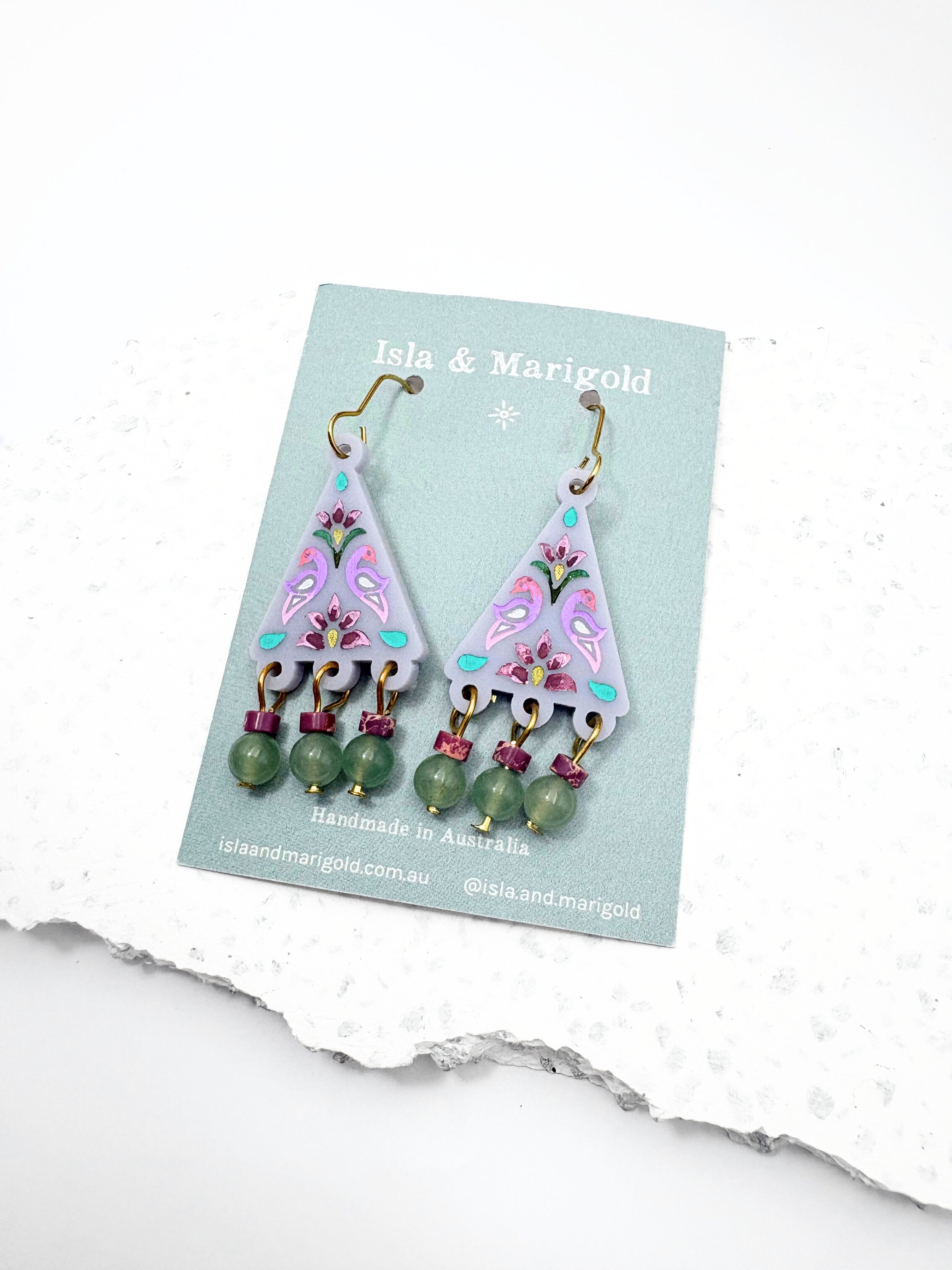 Triangular earrings with floral designs and green beads on a 'Isla & Marigold' card.